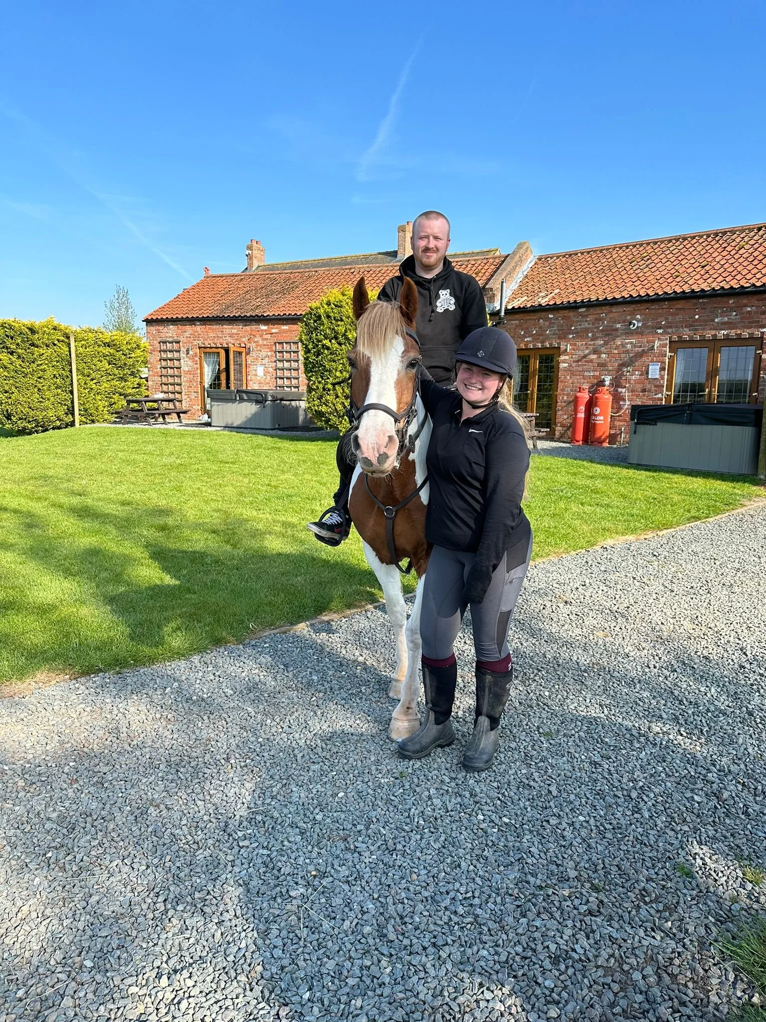 A man and a woman with a horse in a yard with a brick house and a lawn.