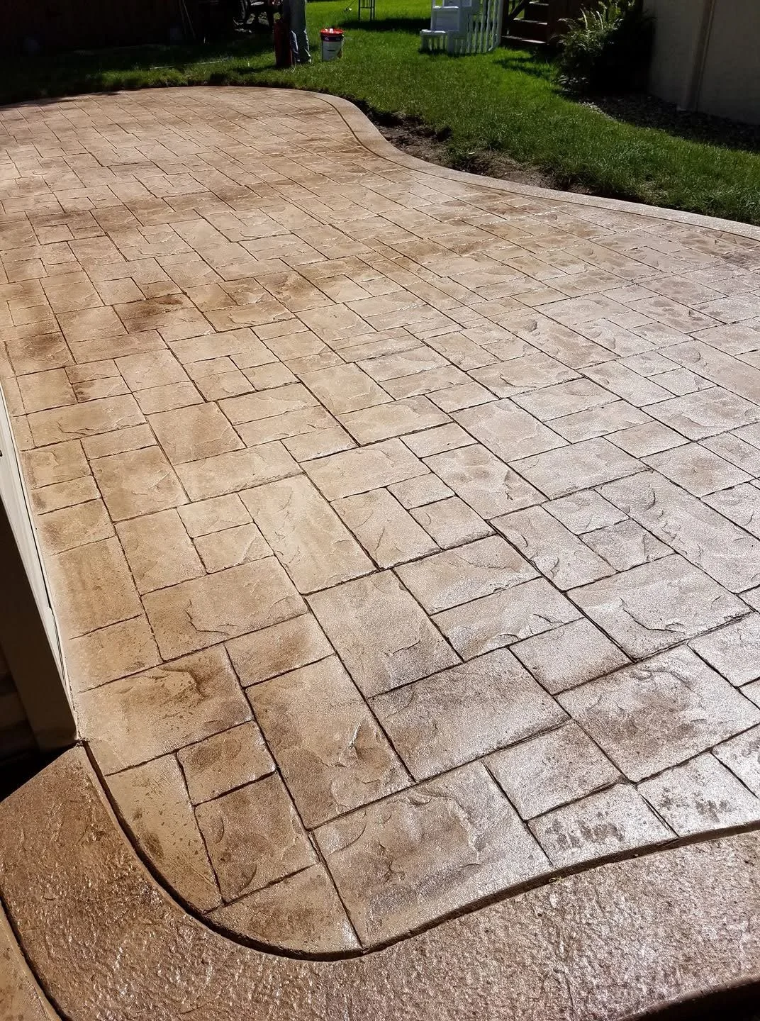 Newly paved stone patio with a curved edge in a backyard, bordered by grass and garden.