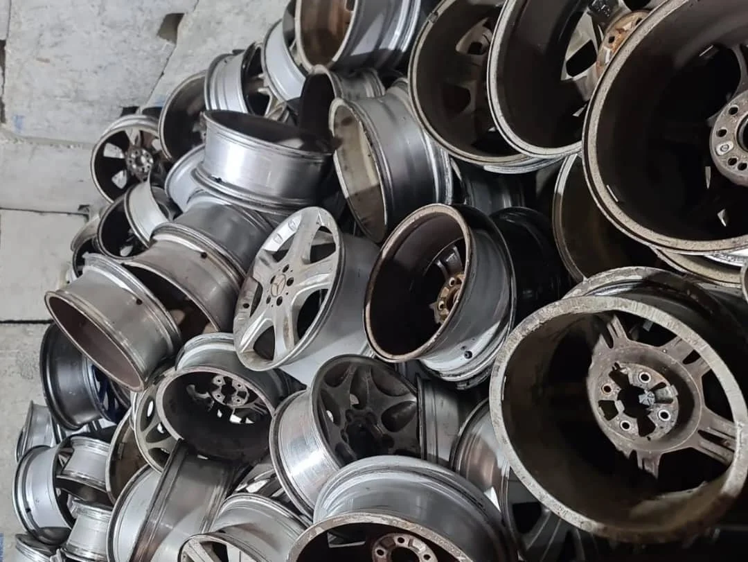 A large pile of used alloy car wheels stacked on a concrete floor.