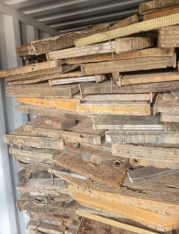 Stack of old, weathered wooden window screens or frames leaning against a metal wall.