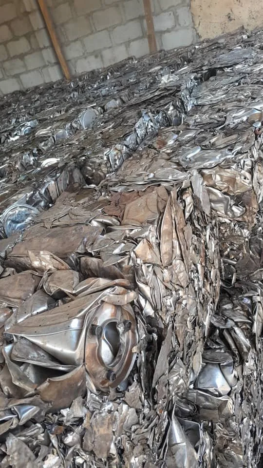 A large pile of crushed and crumpled aluminum cans in a storage area with bare brick walls.