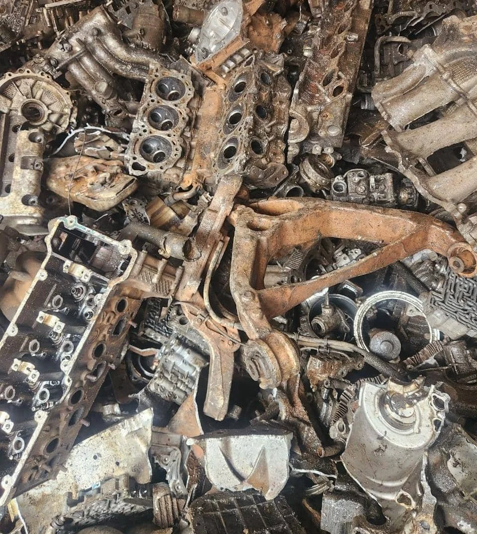 Pile of rusted and used automobile engine parts, including cylinder heads, pistons, and various metal components.