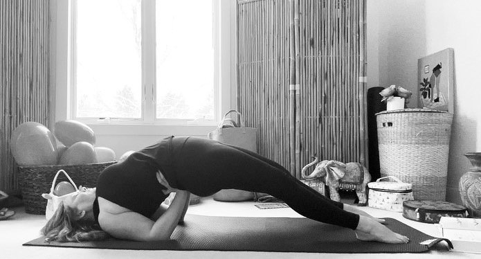 Person practicing yoga in a child's pose on a mat indoors, surrounded by baskets and decorative items.