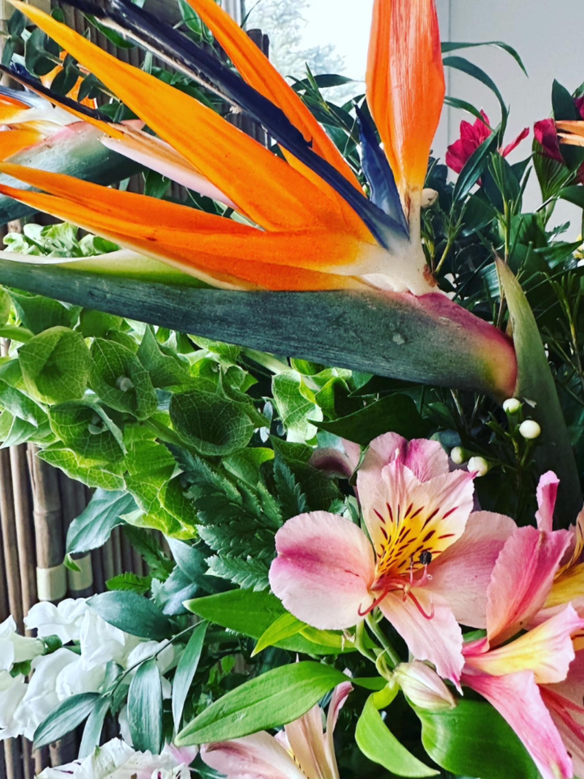 Close-up of a vibrant bouquet with a bird of paradise flower, pink lilies, and various green foliage.