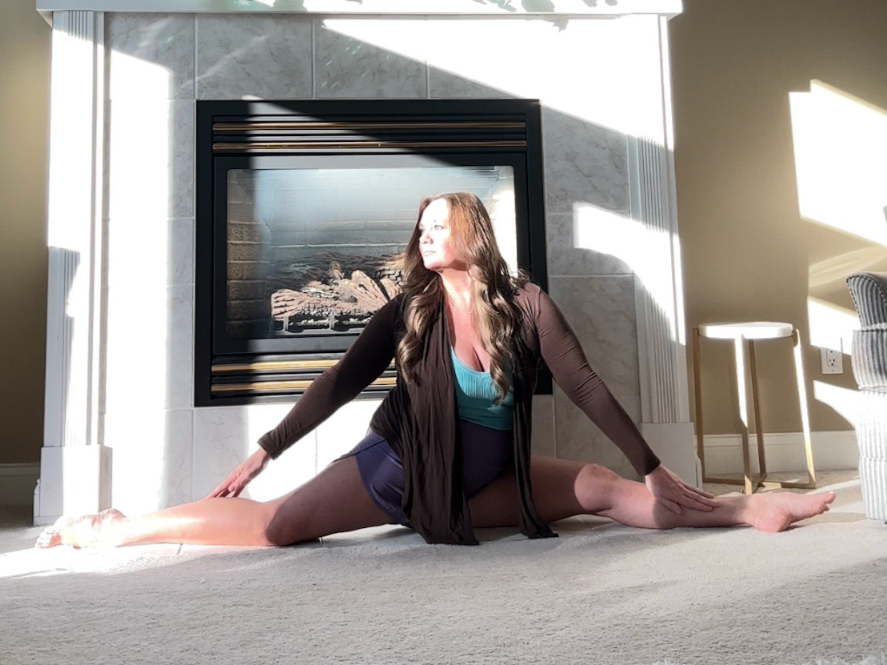 Woman practicing yoga in front of a fireplace in a living room with sunlight streaming in.