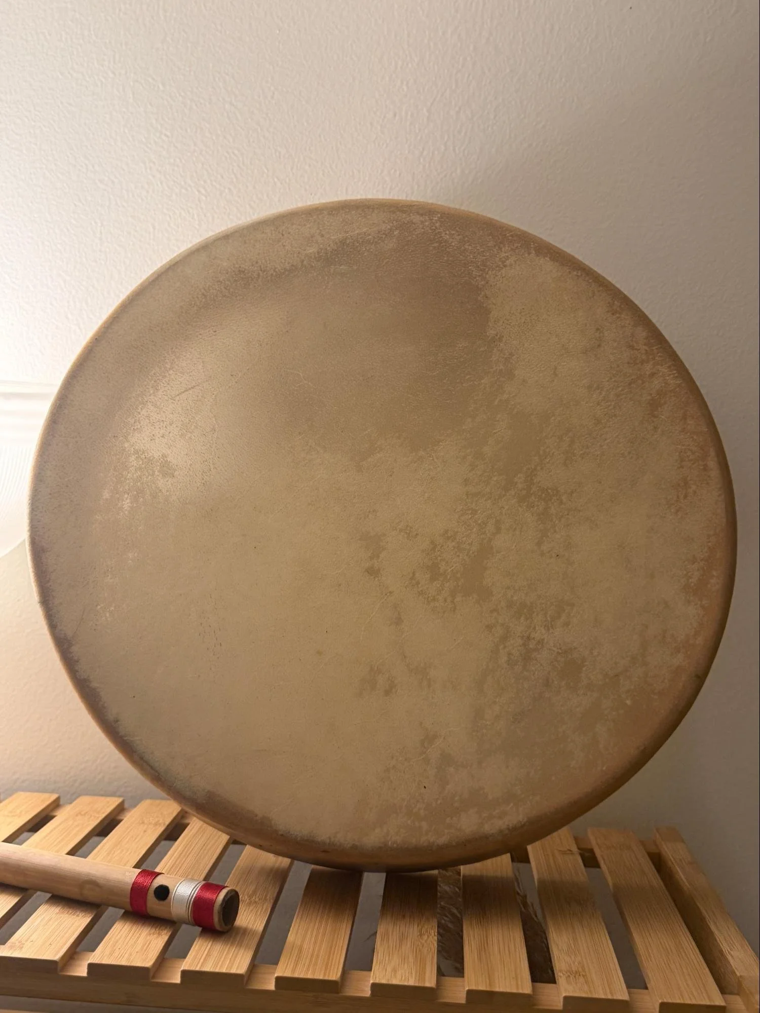 A large round metal plate with a slightly textured surface, placed on a wooden slatted stool with a red and white flashlight in the foreground.