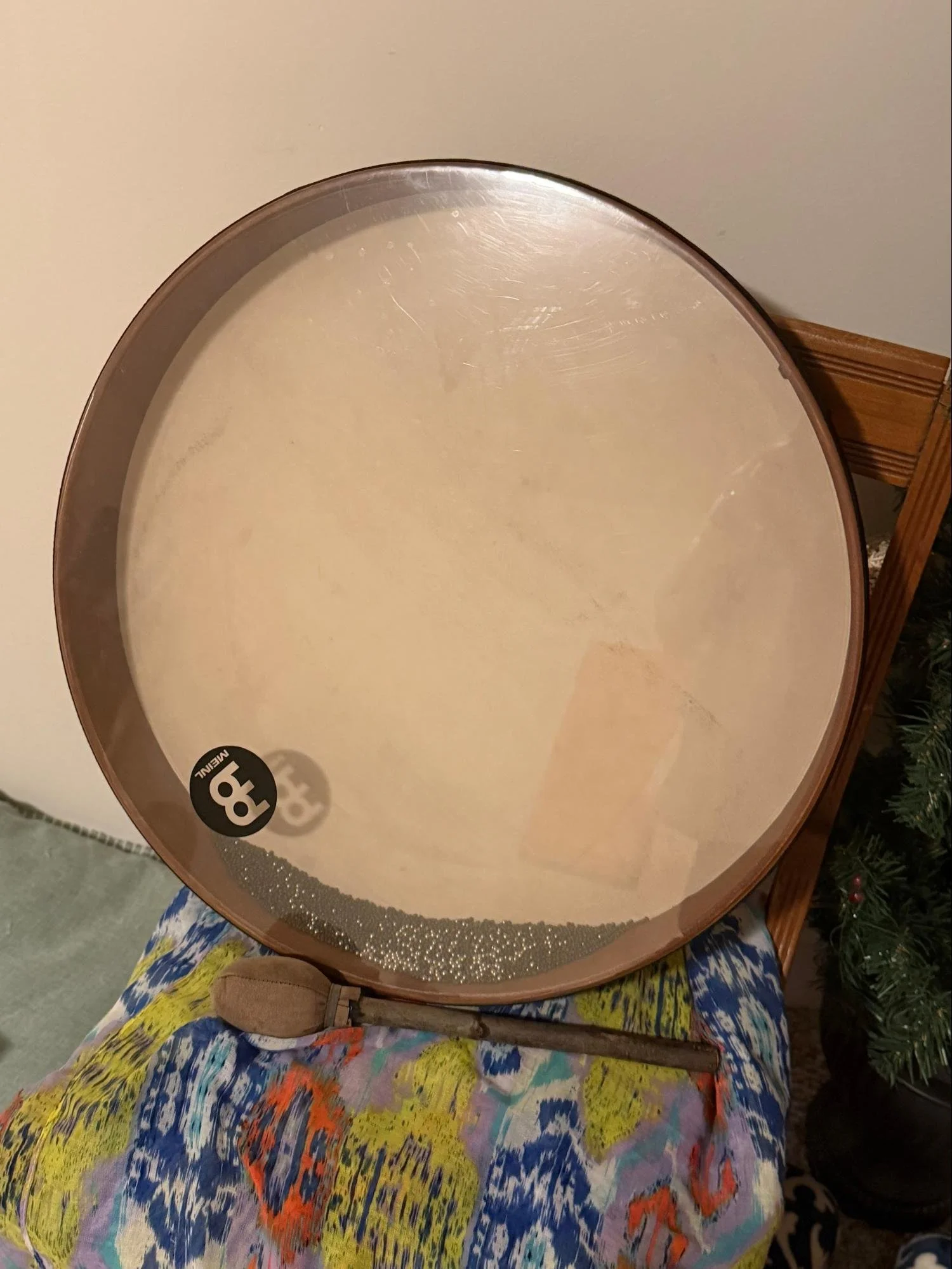 A round mirror with a silver border resting on a wooden stand. The mirror's surface shows some smudges and fingerprints. The mirror is placed on a colorful, patterned fabric tablecloth.