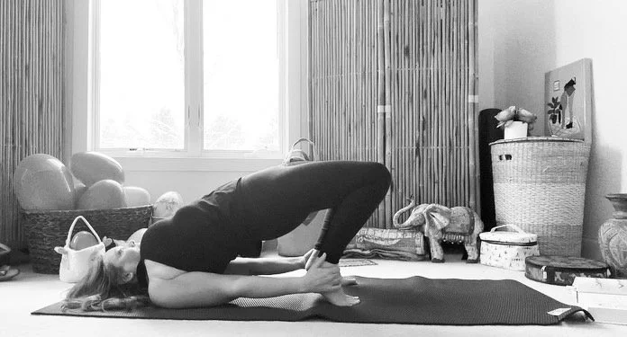 A woman practicing yoga on a mat in a room with large windows and various decorative items.