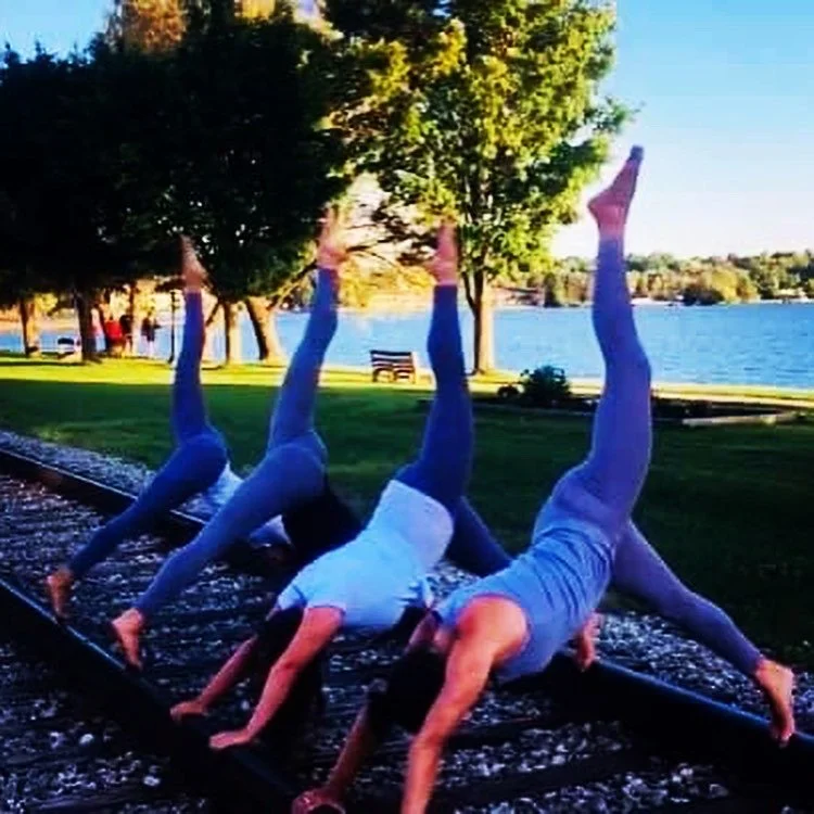 People practicing yoga outdoors near a lake with trees and a park bench.