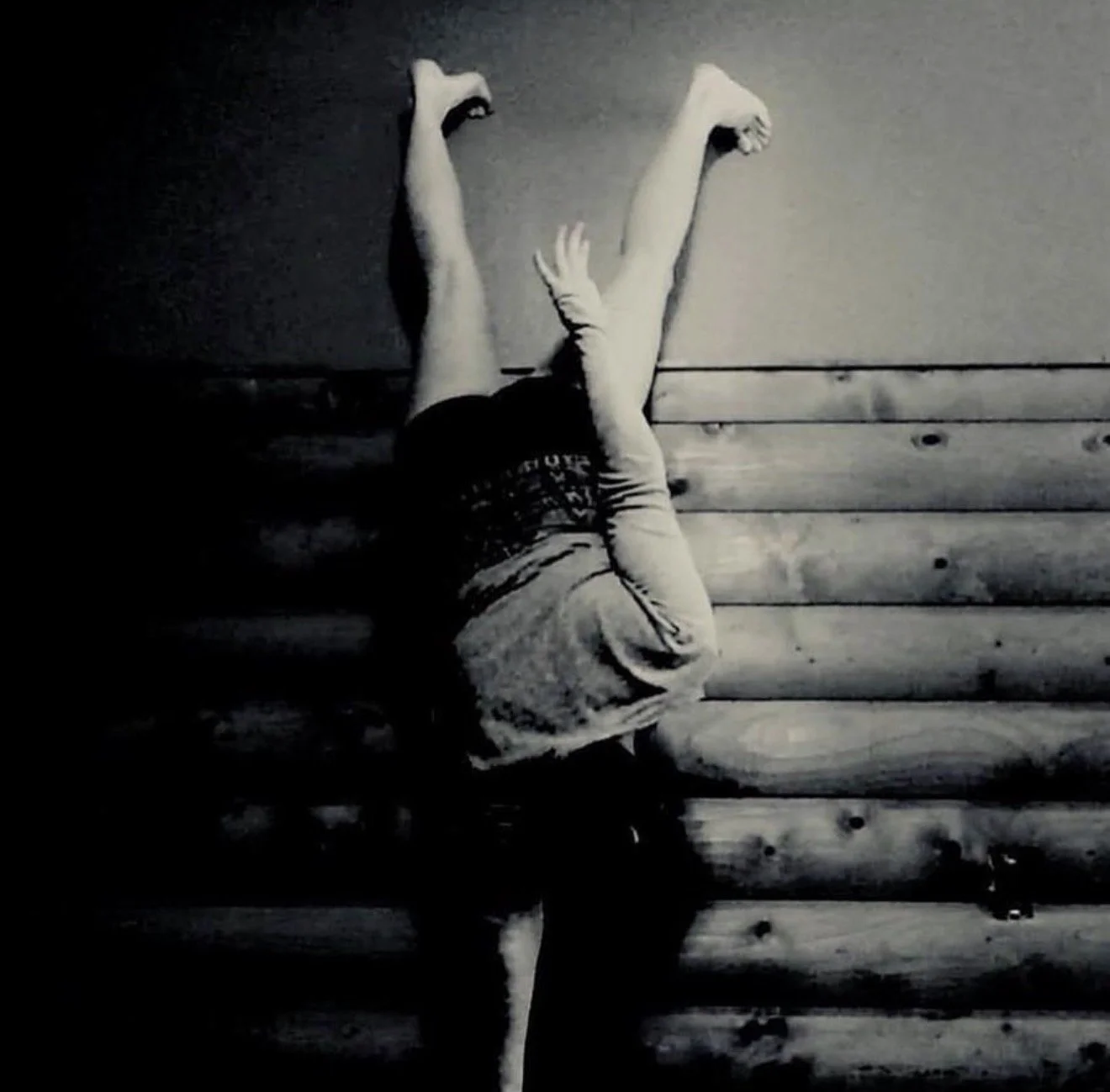 Child crawling upside down on a wooden floor, with bare feet and wearing shorts and a t-shirt.