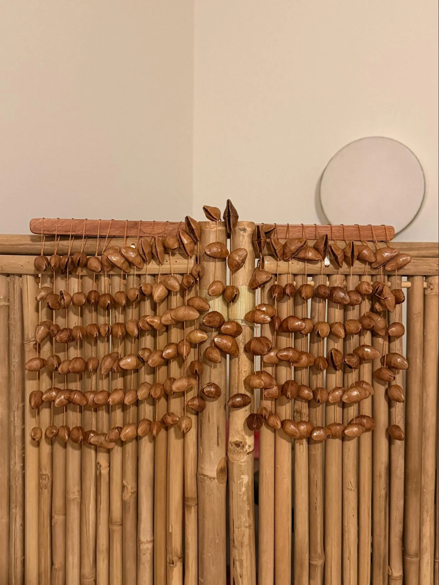 Decorative wooden and bamboo wall art with wooden beads hanging from a horizontal wooden rod against a beige wall.