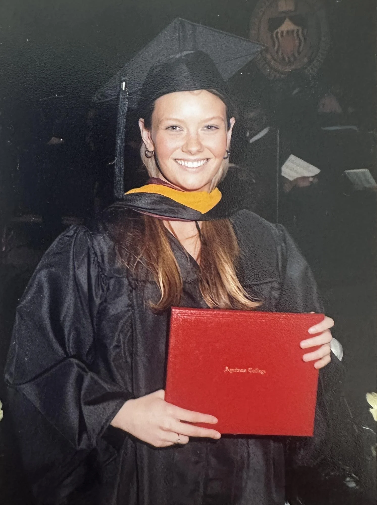 Woman in graduation gown and cap holding a red diploma cover.