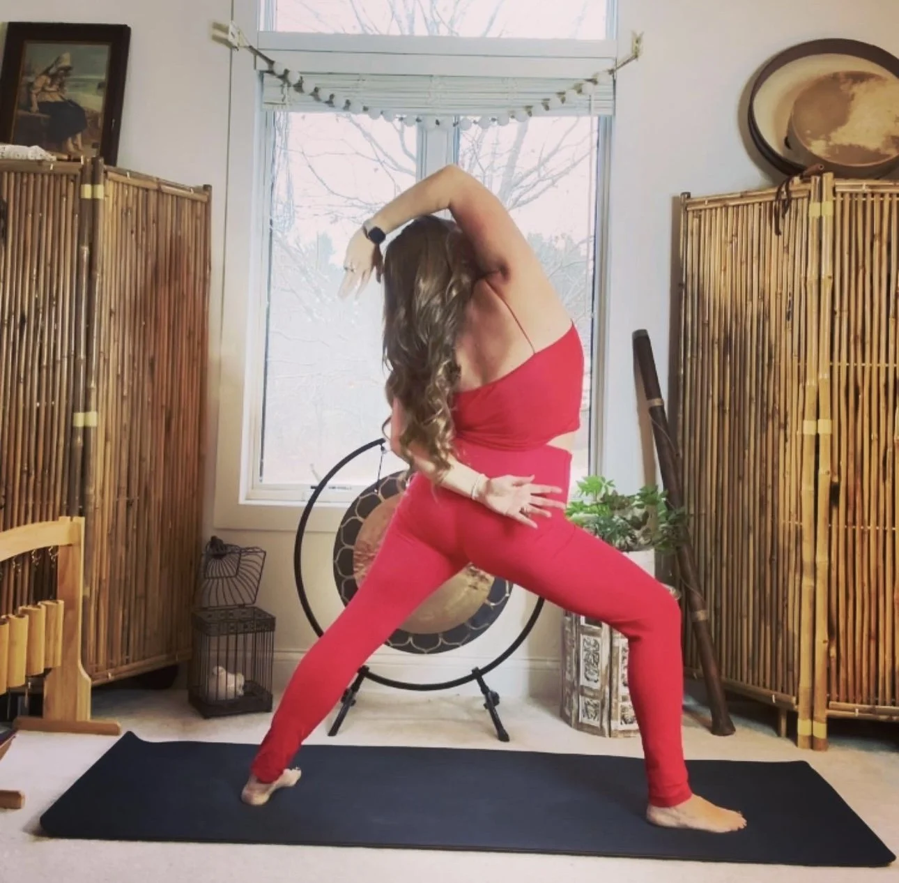 Woman practicing yoga in a red outfit in a room with bamboo screens and decor.