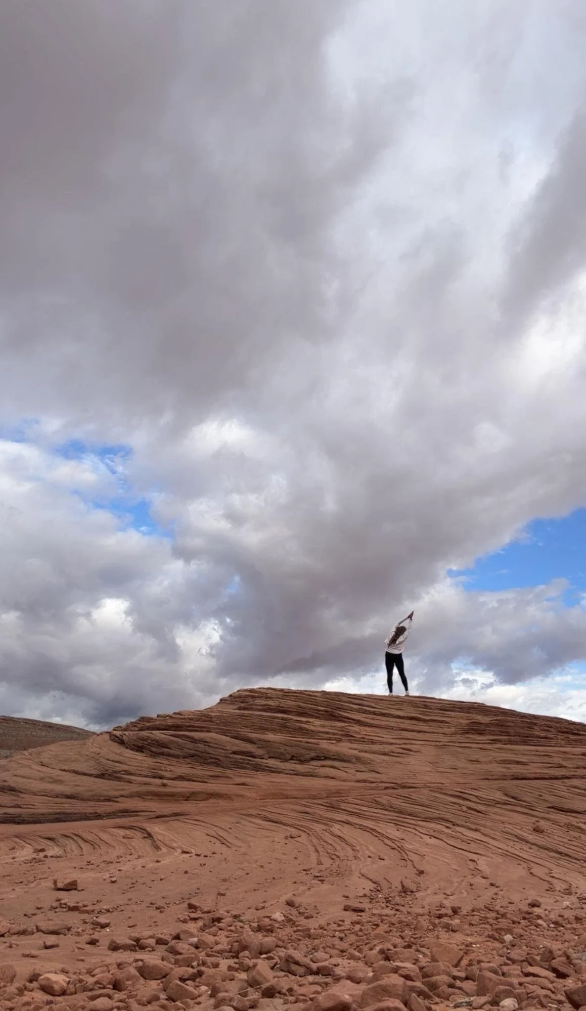 A person standing on a rock formation in a desert landscape, with a cloudy sky overhead.