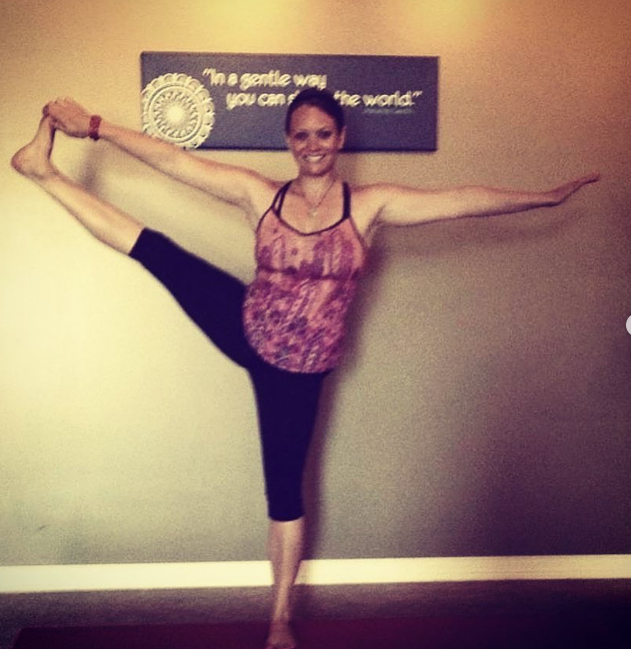 A woman performing a dance pose with one leg raised high to the side and her arms extended horizontally, standing against a beige wall with a motivational quote in the background.
