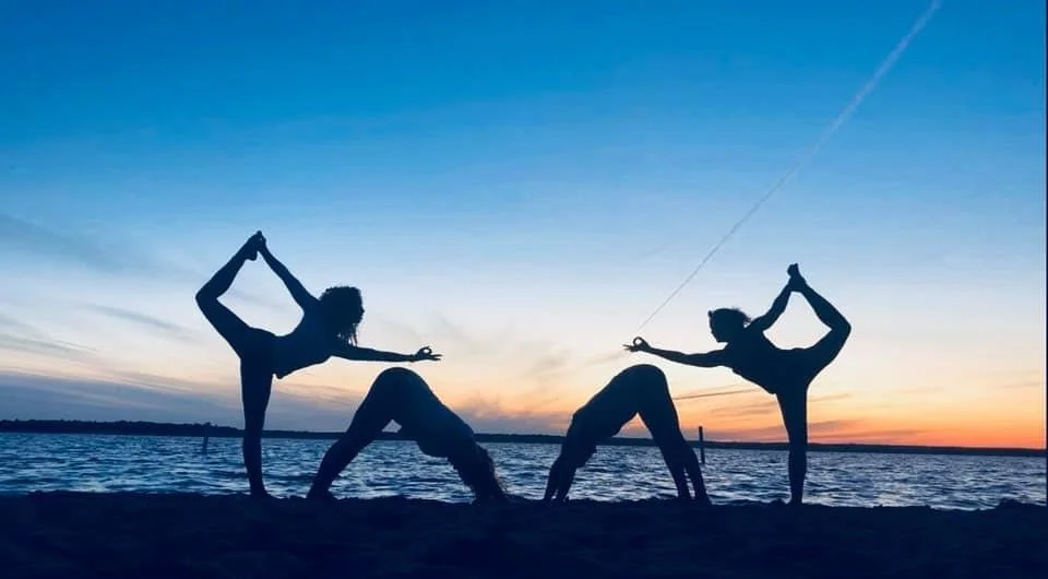 Four people performing yoga poses on the beach at sunset.