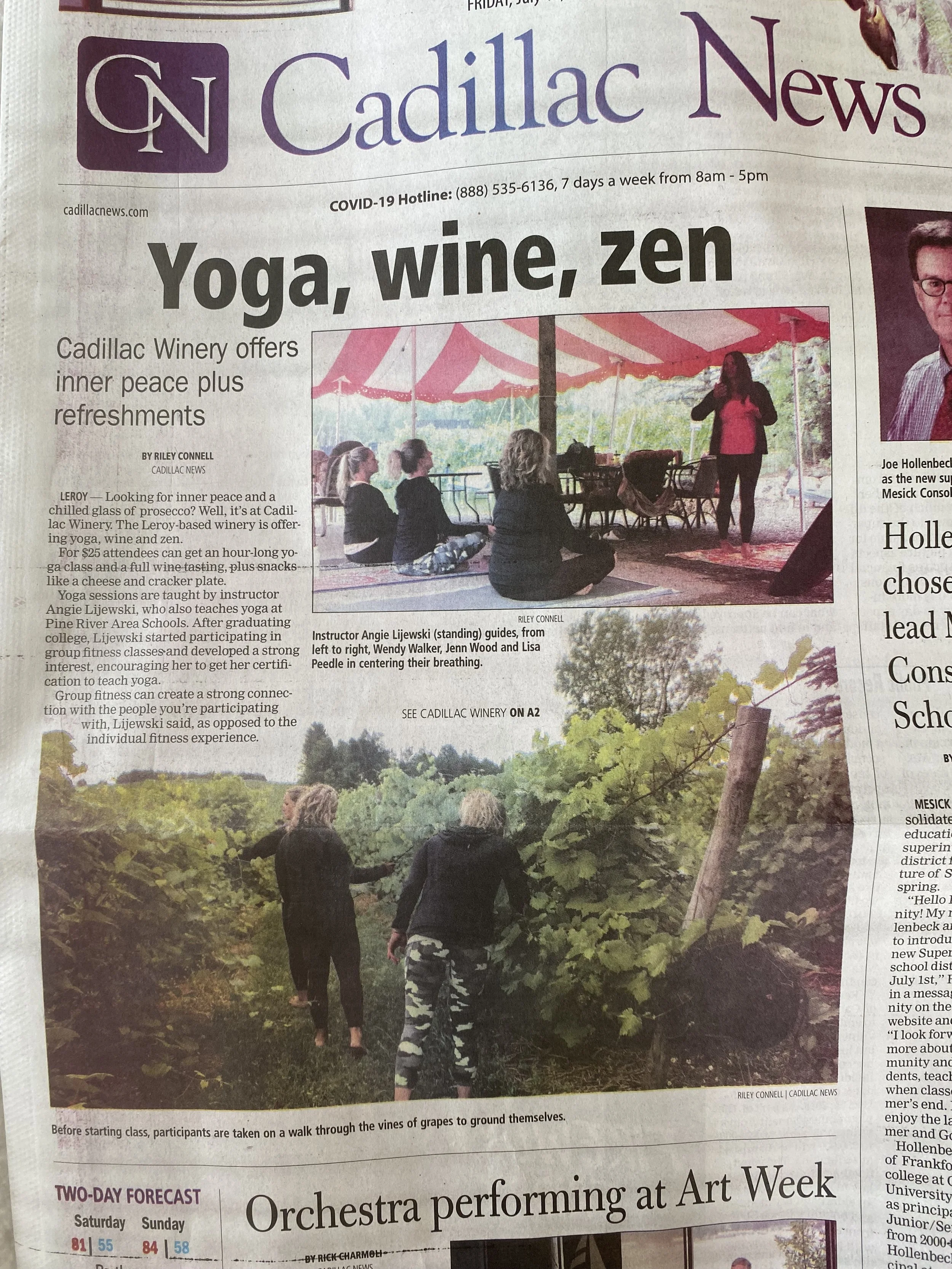 People attending a yoga class outdoors under a pink tent, with some seated and one instructor standing and guiding breathing, surrounded by trees.