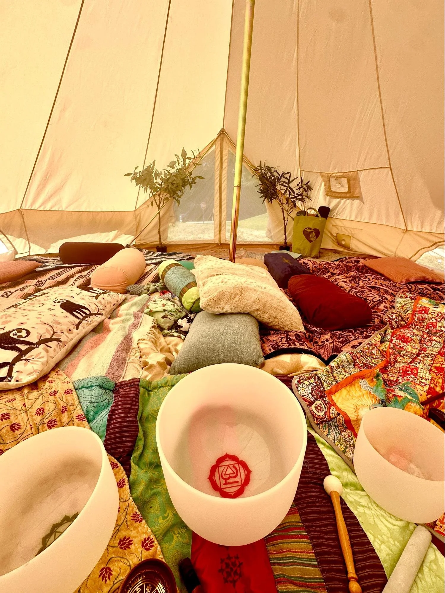 The inside of a large outdoor tent with a low table covered with colorful cloth, surrounded by round white cups, pillows, plants, and miscellaneous objects.