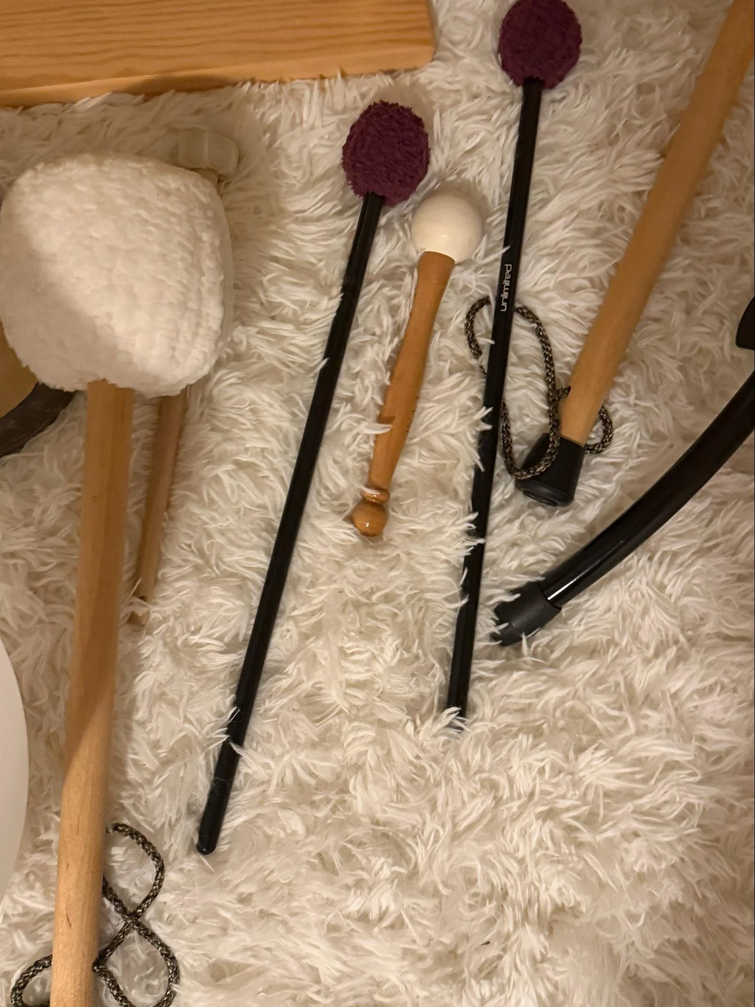 A cozy bedroom setting with a fluffy white rug on the floor, displaying a pair of white slippers with fuzzy soles, and four walking sticks or canes with different handles including one with purple fuzzy balls, one wooden, and one with a chain handle,