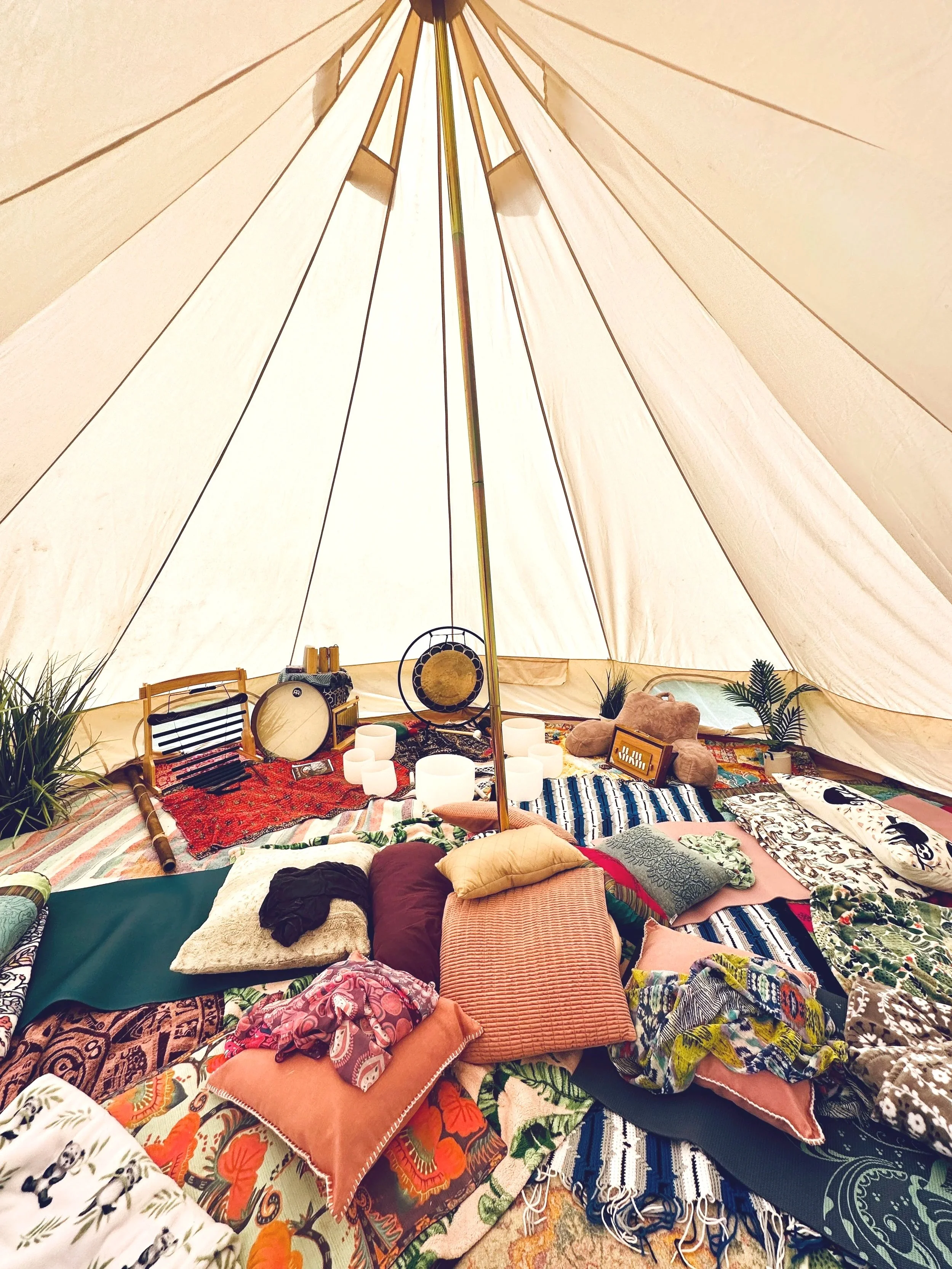 The interior of a teepee tent decorated with various pillows and rugs, musical instruments, candles, and potted plants.