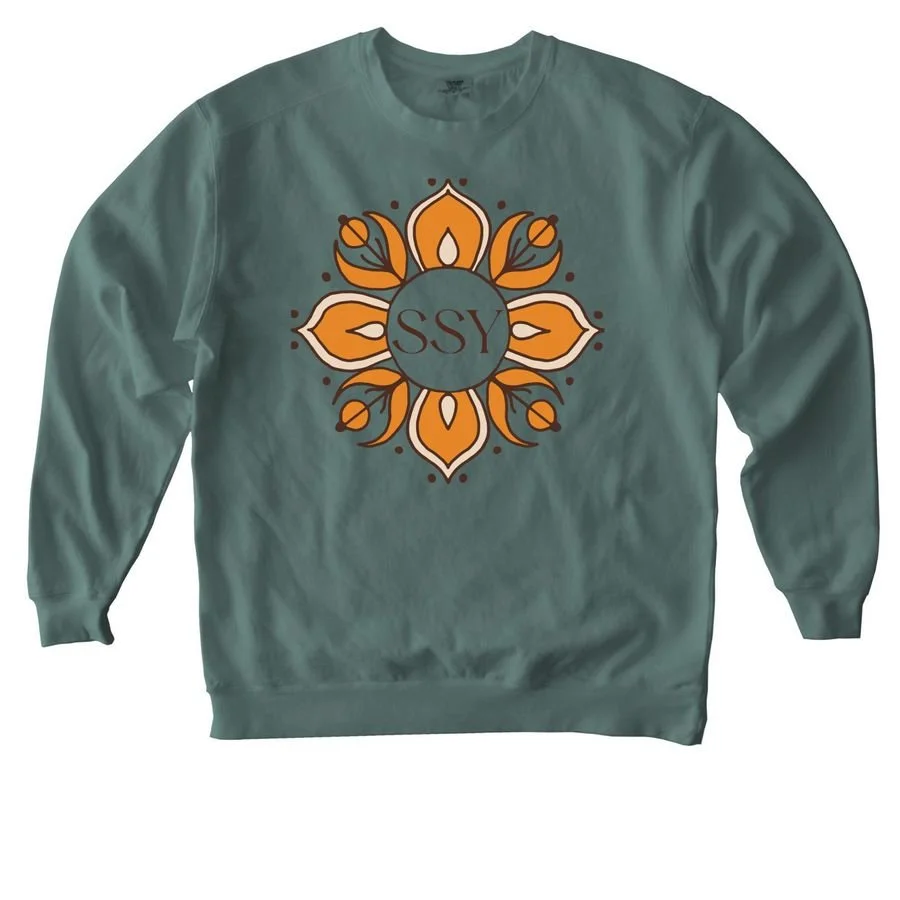 A teal sweatshirt with a central circular design featuring orange, white, and yellow floral patterns around a blue circle with the letters 'SSY' inside.