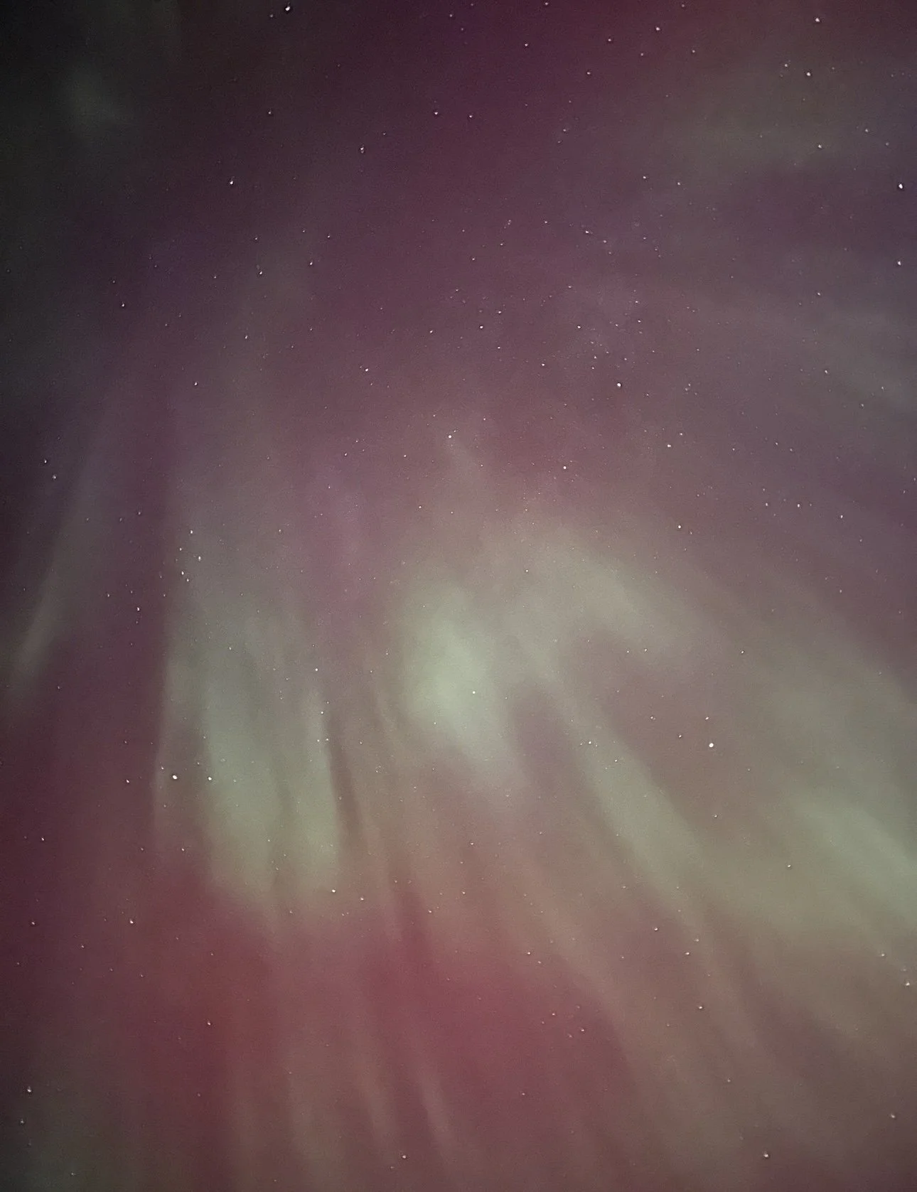 A blurry image of the night sky with stars, showing some green and purple light streaks, possibly visible auroras or lens effects.