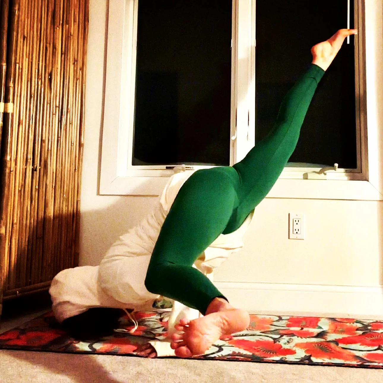 Person practicing yoga in a headstand position on a yoga mat inside a room at night.