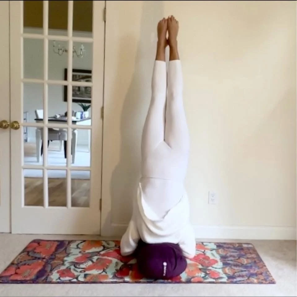 Person doing a headstand yoga pose against a wall in a room with a door and a decorated mat.