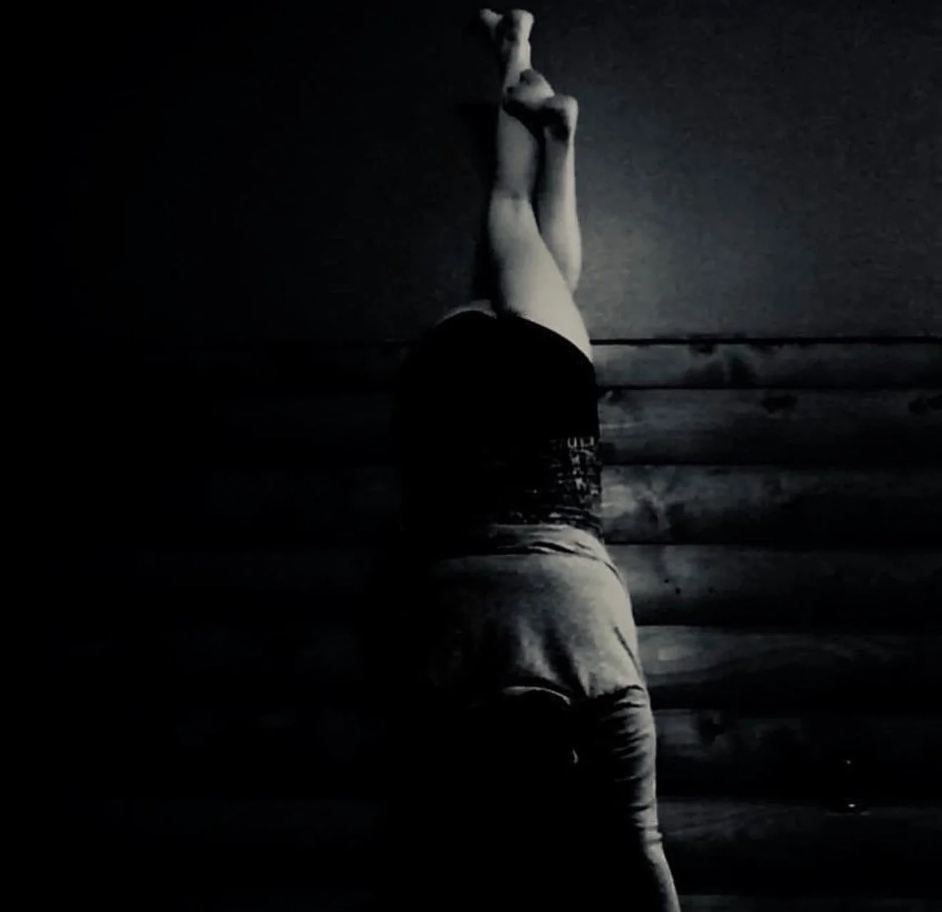 Person performing a handstand against a wall in a dimly lit room.