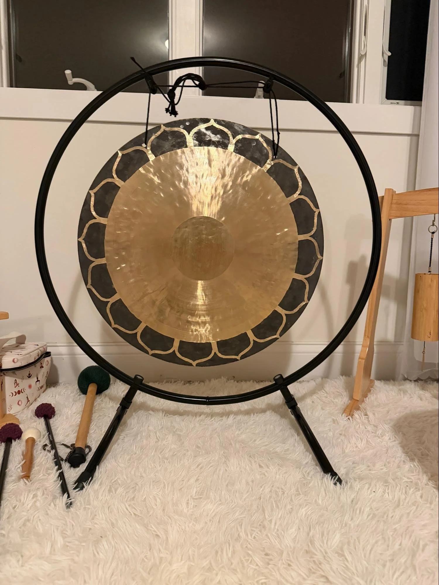 A large gong with a black frame hanging from a circular stand, placed on a white fluffy rug inside a room.