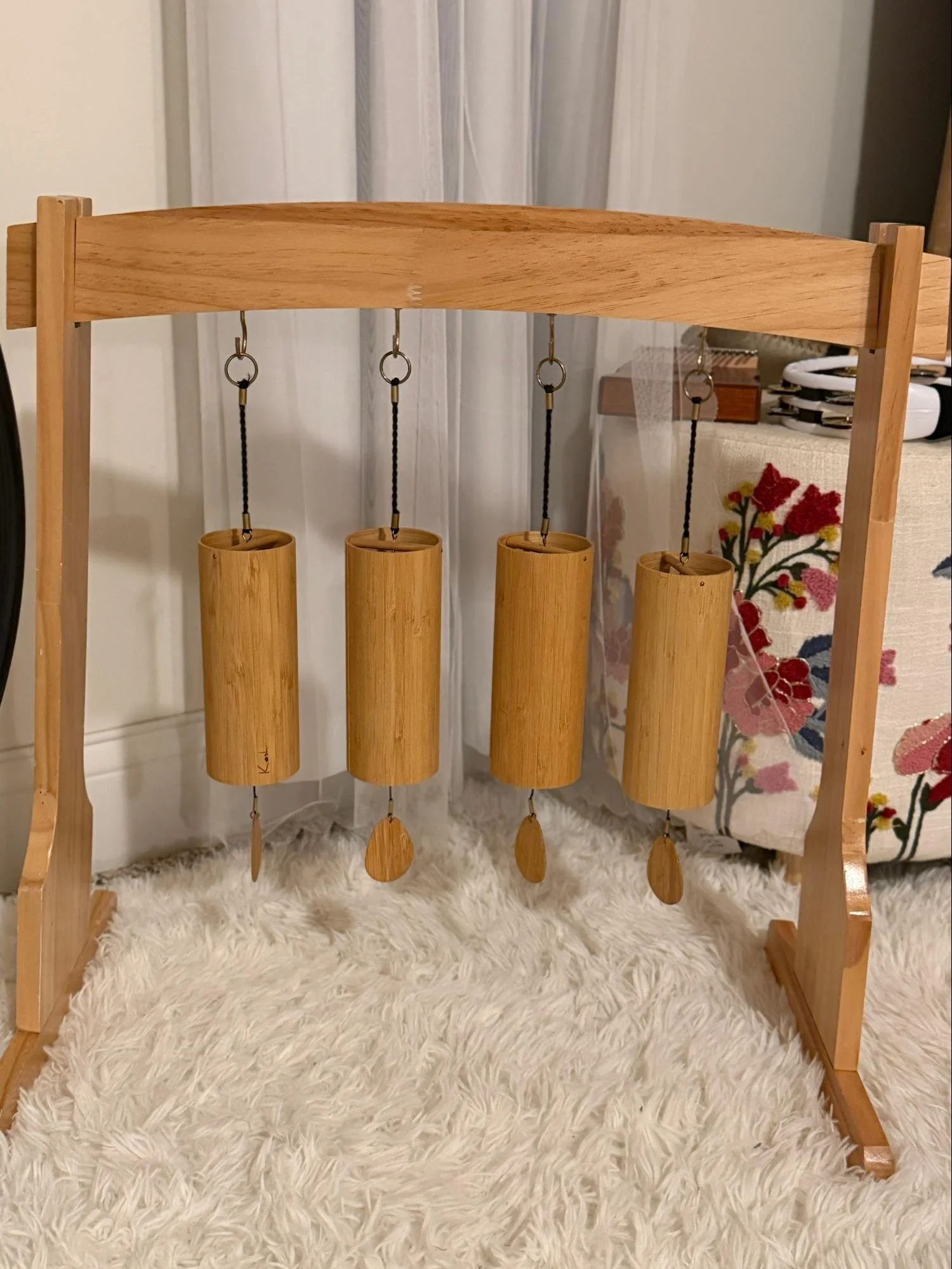A wooden wind chime with four bamboo tubes hanging from a wooden frame, set on a fluffy white rug.