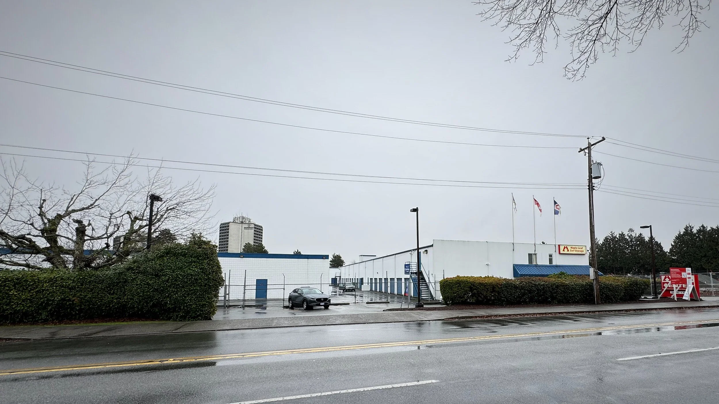 A view of a commercial storage building surrounded by bushes and trees, on a rainy day.