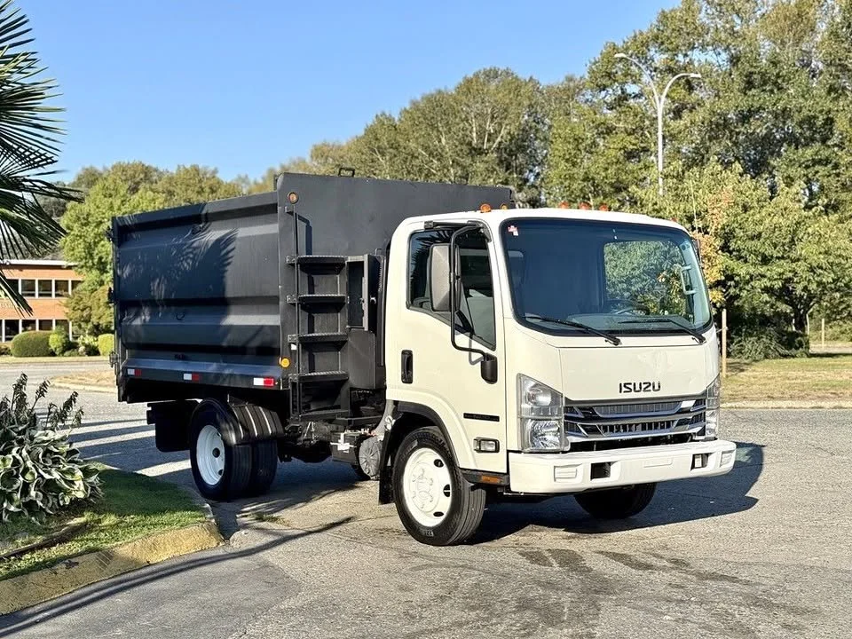 Isuzu box truck parked on a street with trees and a building in the background.