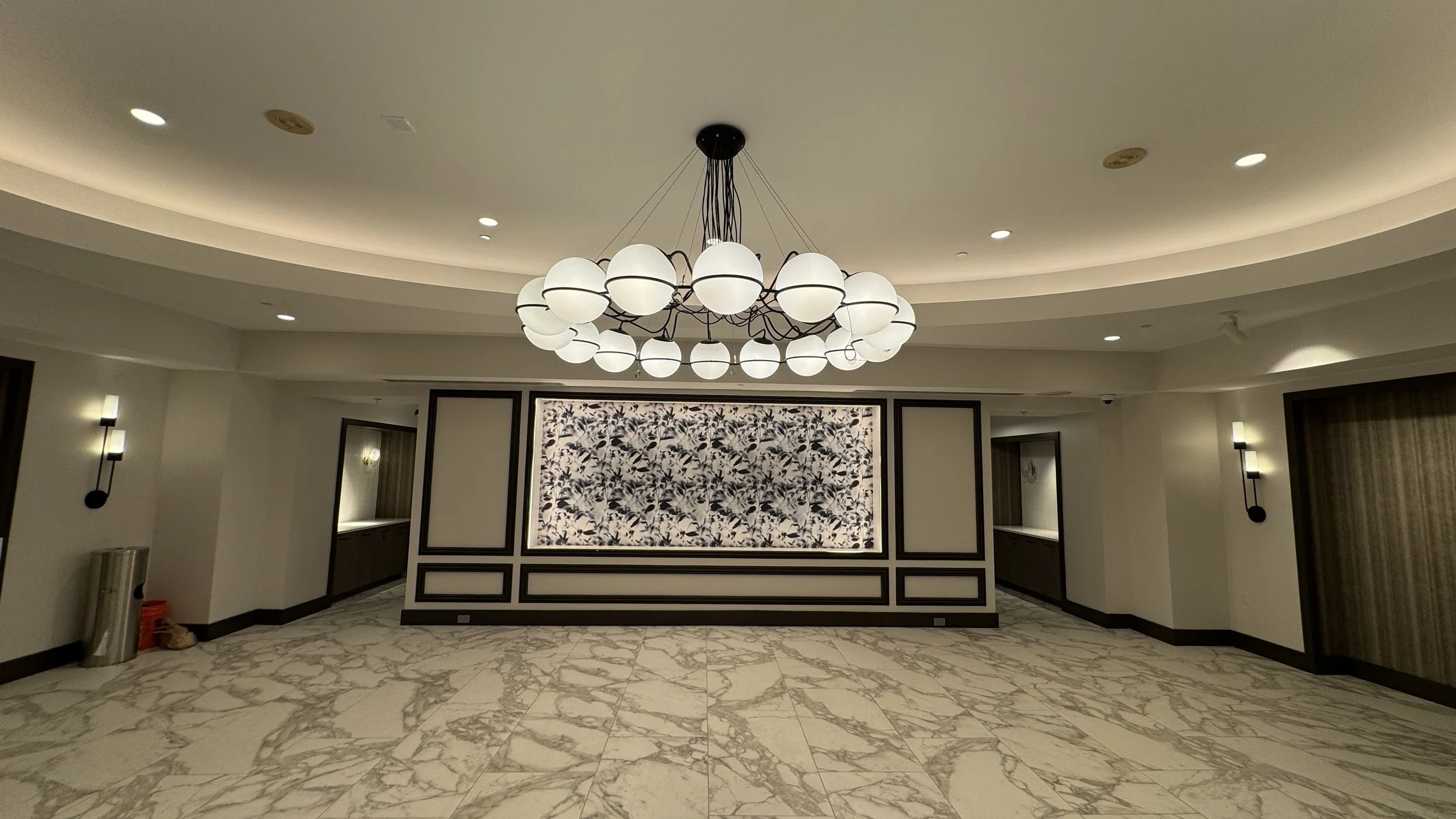 Empty elegant hotel lobby with a modern chandelier, marble floors, and decorative wall panels.