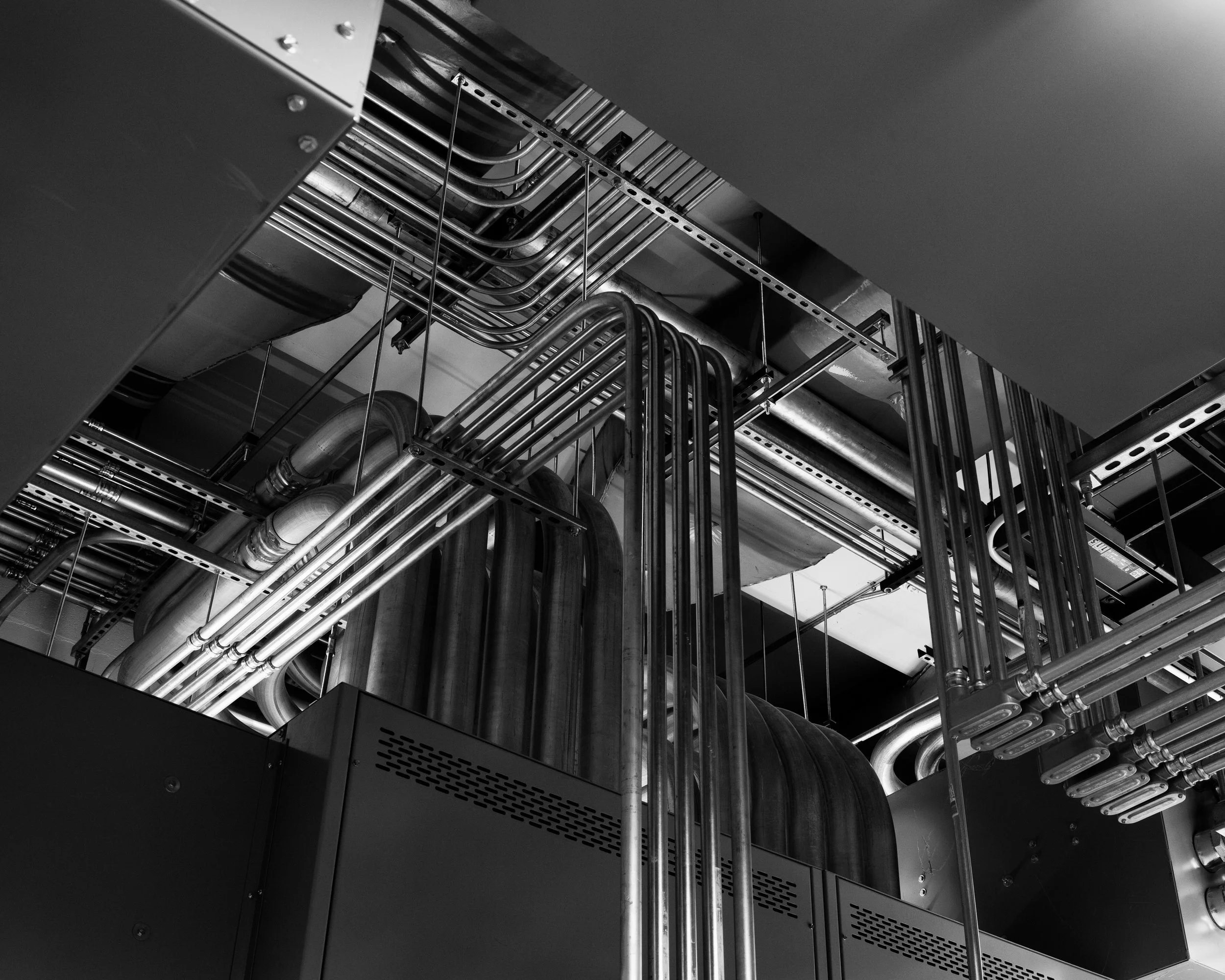 Black and white photo of industrial pipes and machinery in a mechanical room or facility.