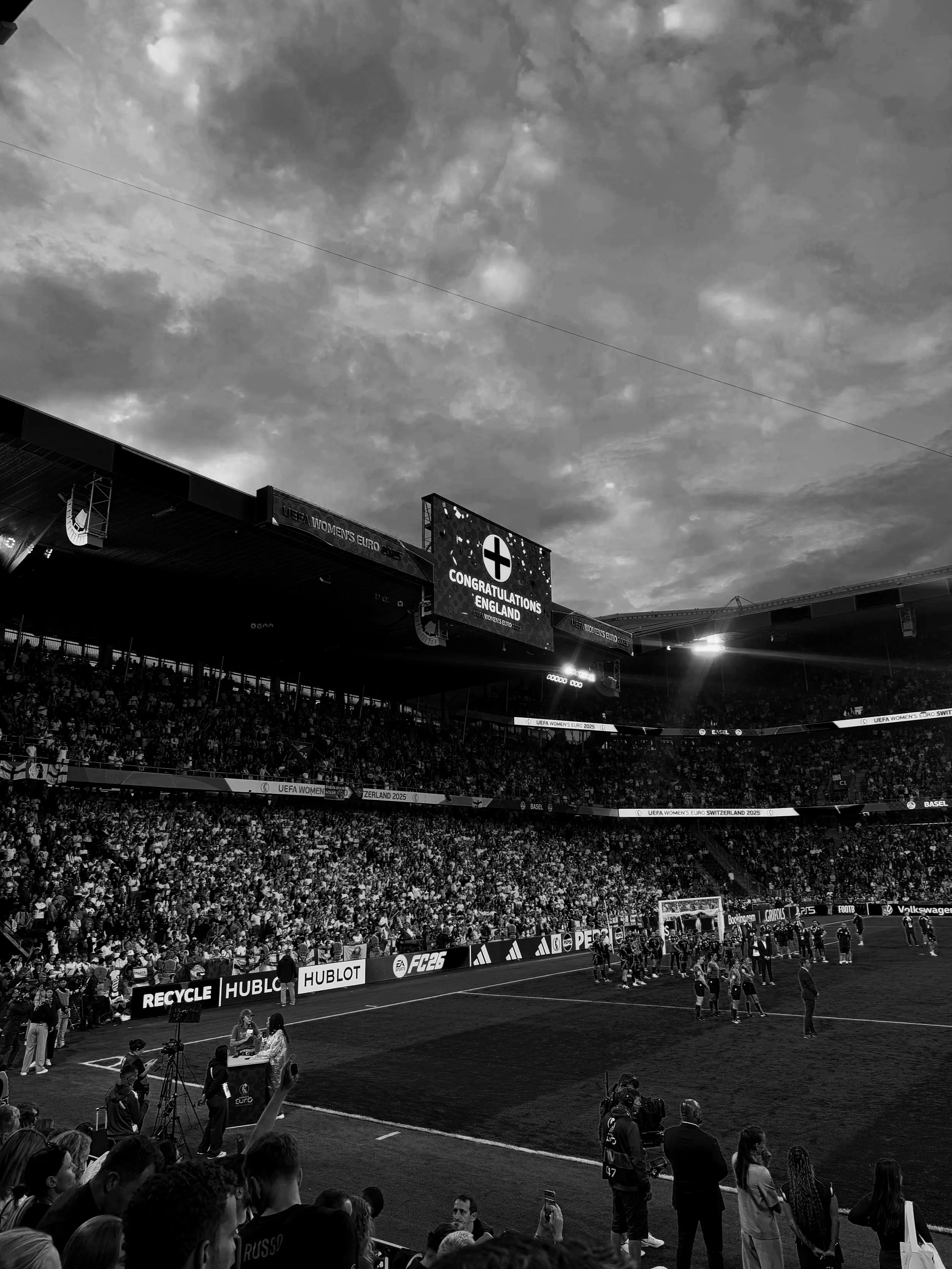 A packed soccer stadium filled with spectators, with players on the field and a large digital screen displaying a congratulatory message for England.
