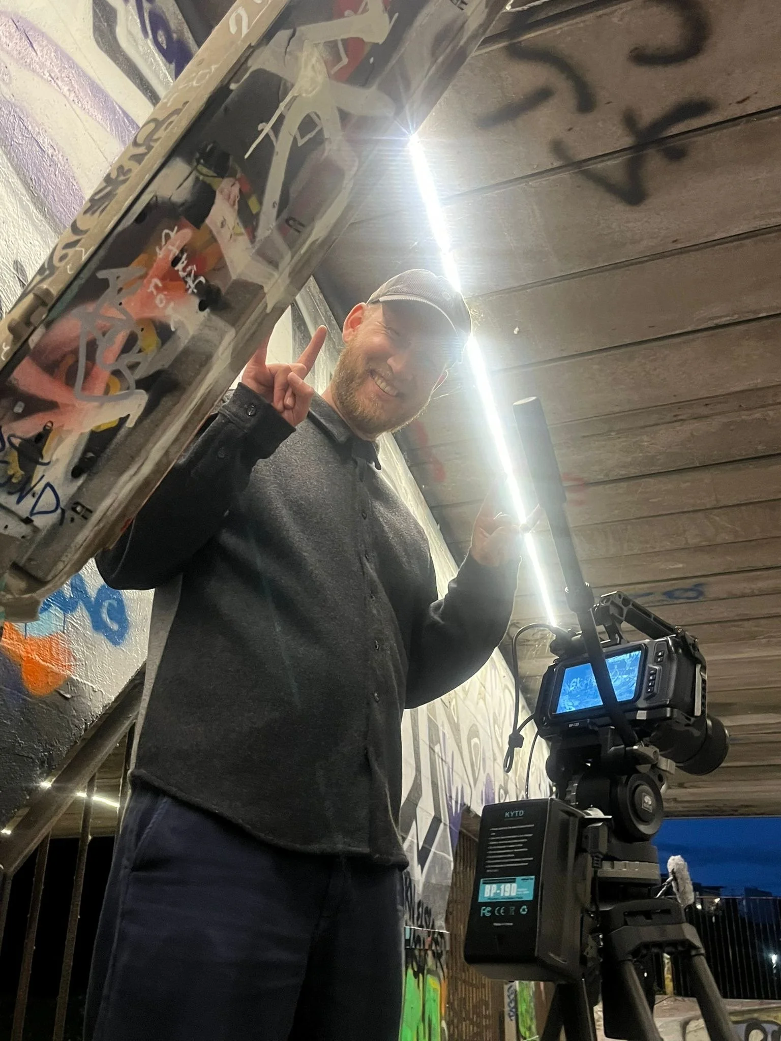 A film crew recording people at a dining table during a gathering, with a woman smiling and others clapping or laughing, seen through a camera monitor.