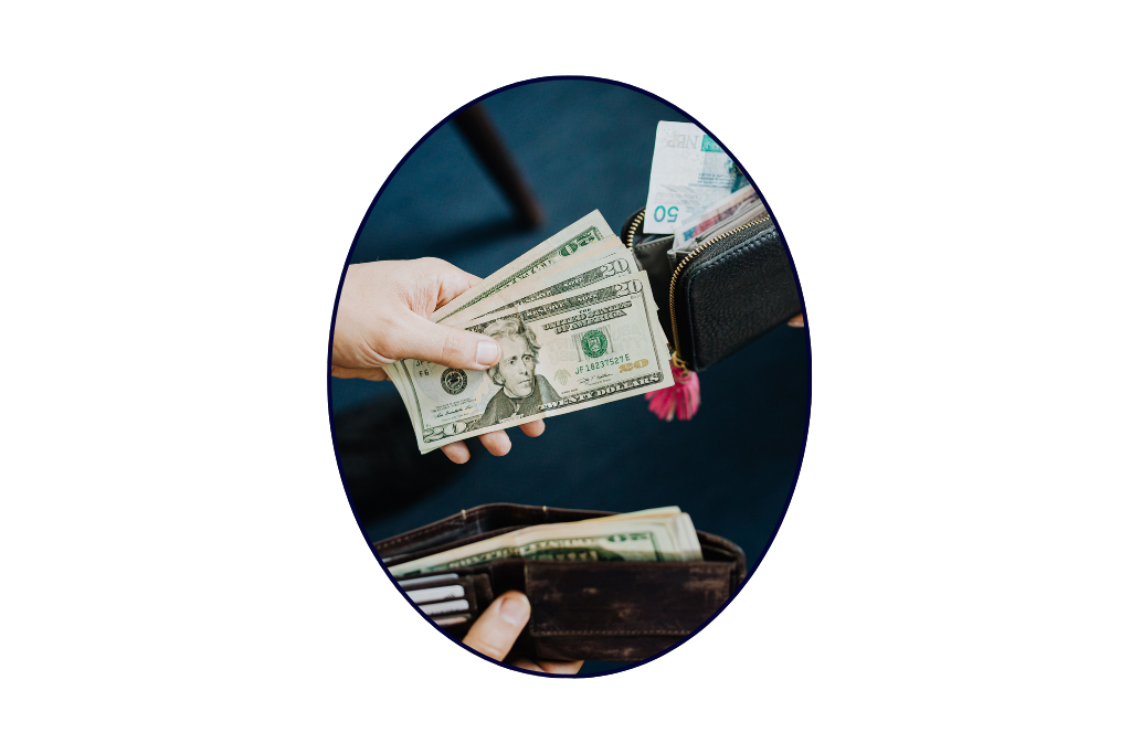A person is handing over US dollar bills to another person who is holding a black wallet with cash inside.