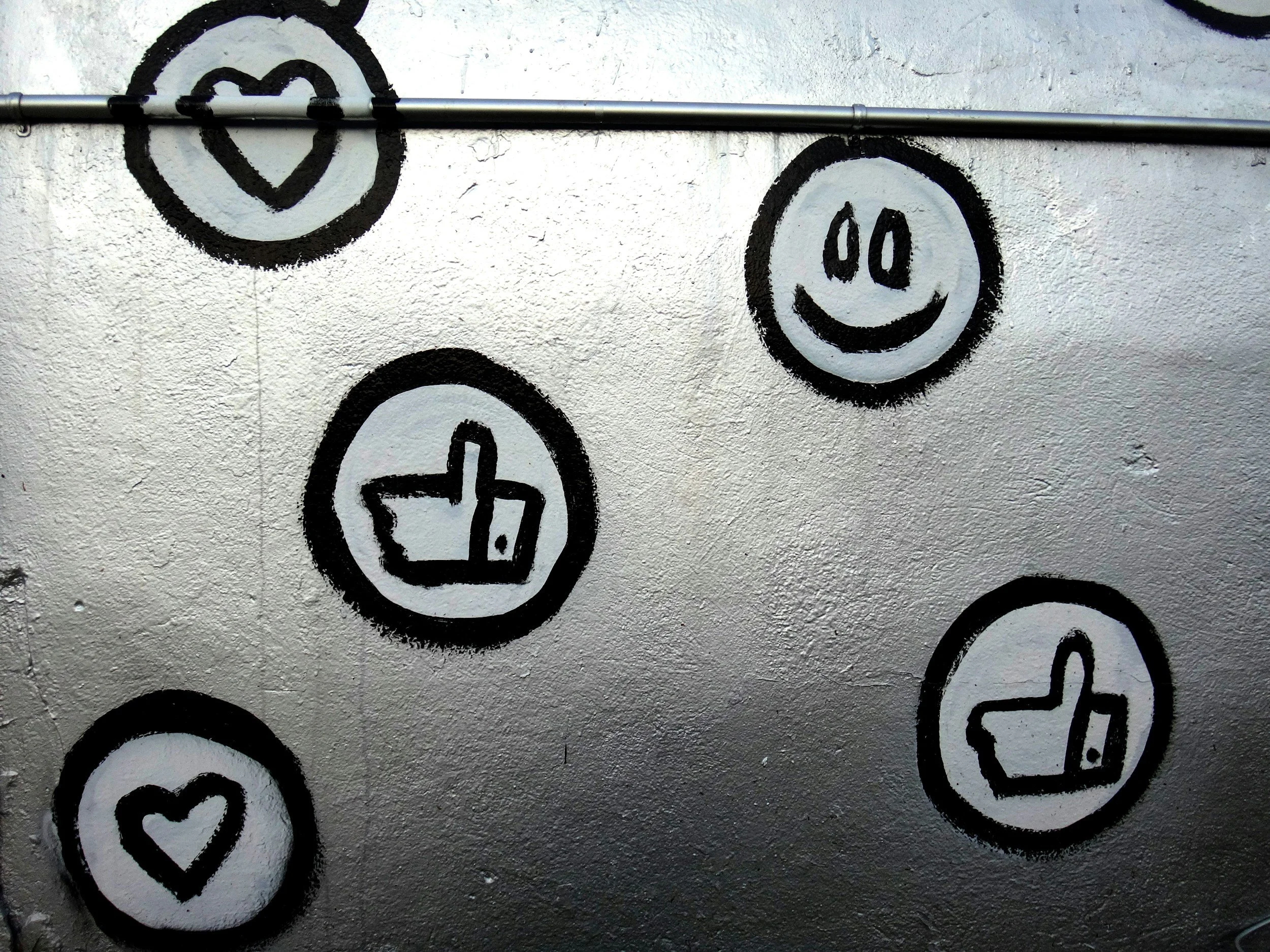 Wall with black outlines of smiley faces and thumbs-up icons painted on a white textured wall.