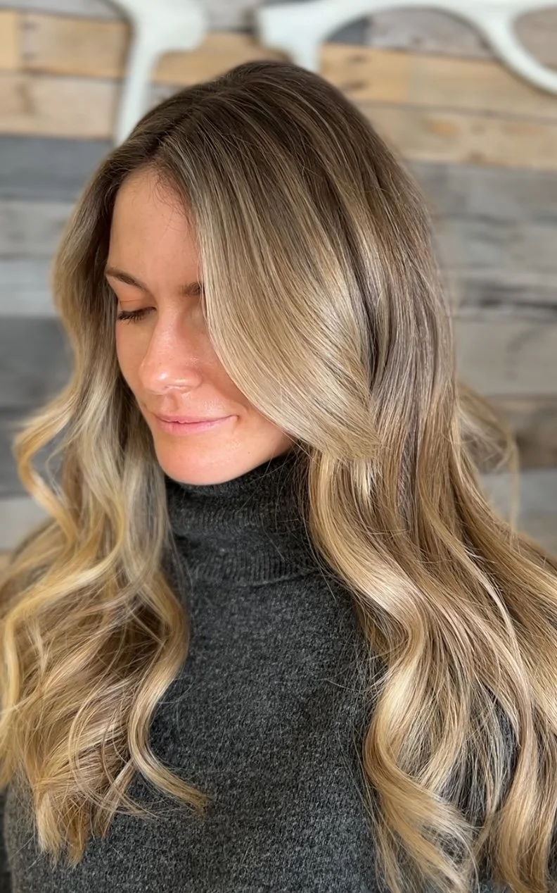 A woman with long, wavy, blonde hair wearing a dark gray turtleneck sweater with her eyes closed.