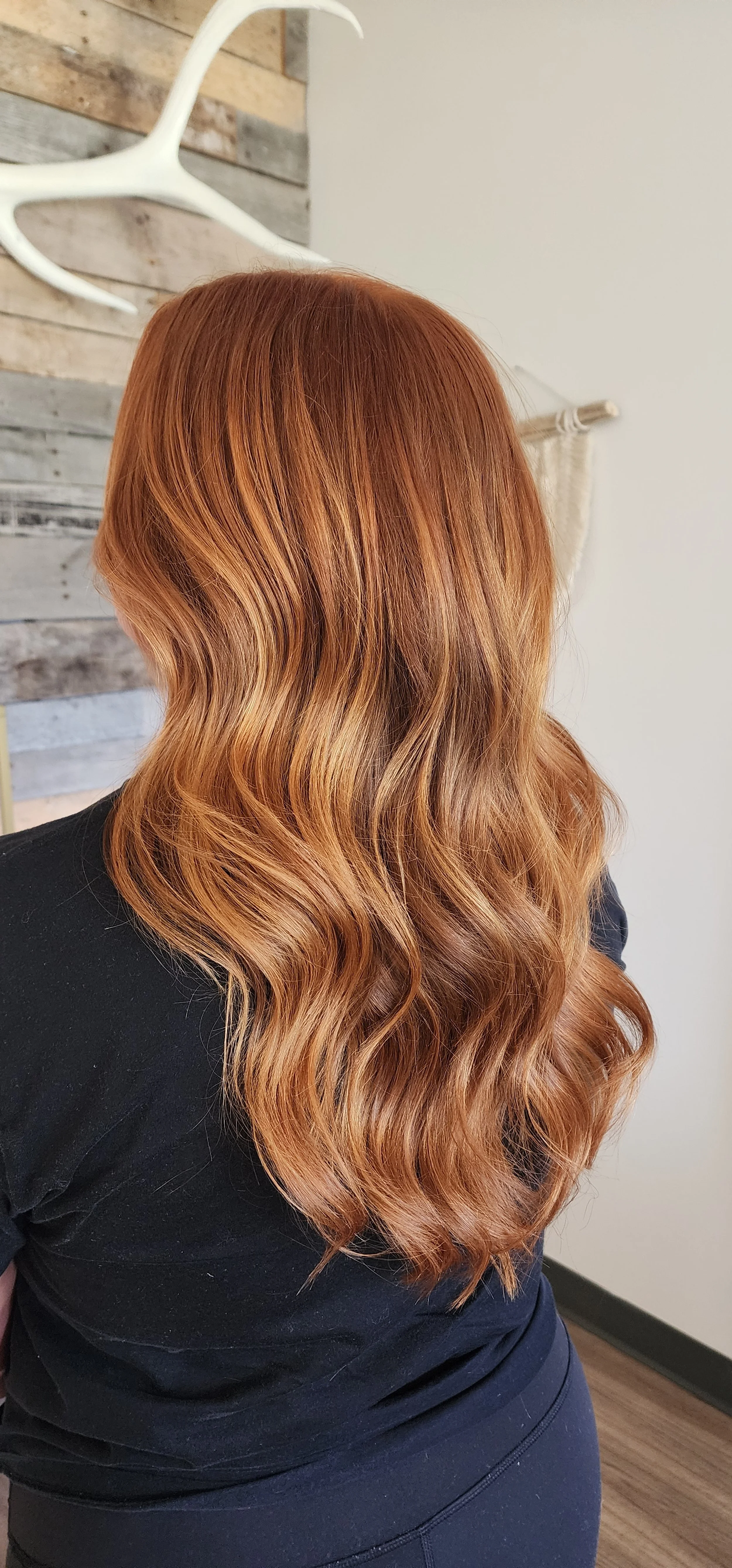 Back view of a woman with long, wavy, reddish-brown hair in a salon or home setting.