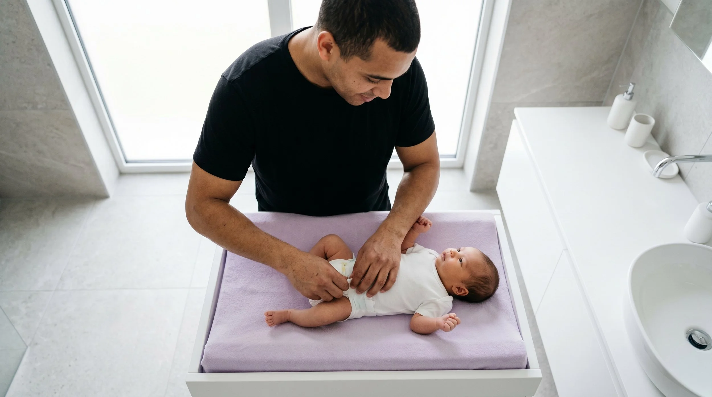 A man changing a baby's diaper on a changing table in a bathroom.