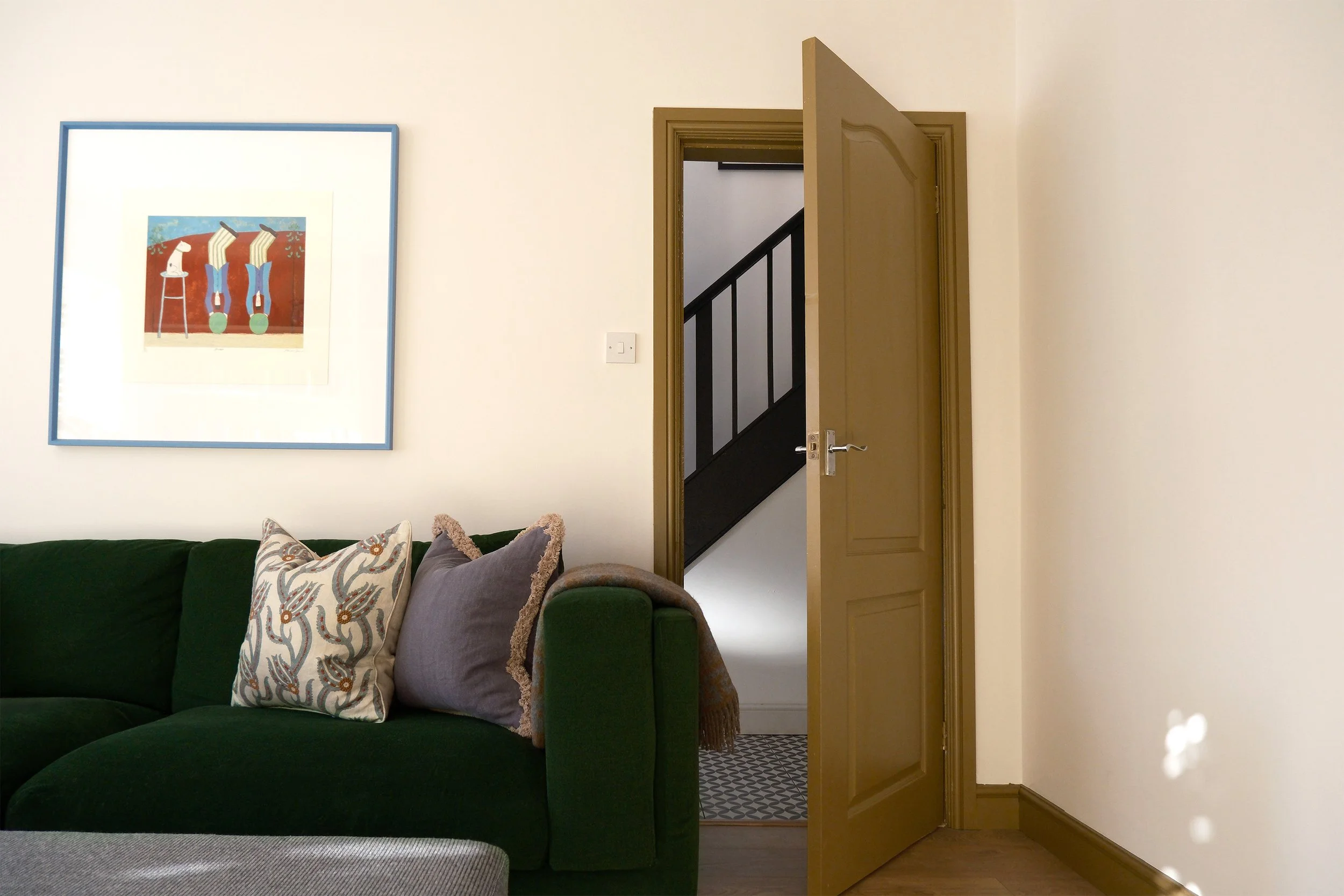 Living room with green sofa, decorative pillows, an open doorway leading to a staircase, and artwork on the wall.