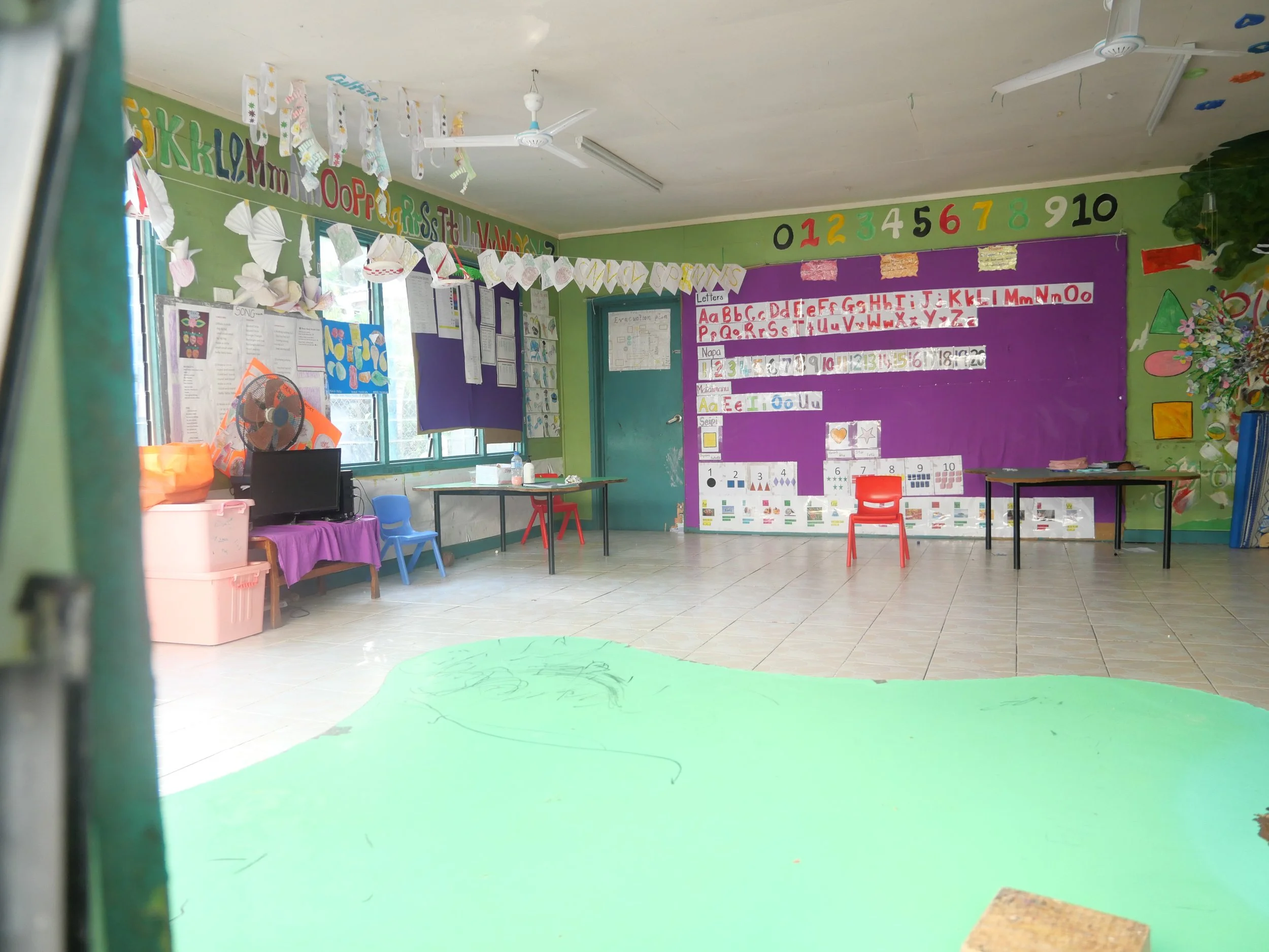 Colorful preschool classroom with alphabet and number displays, small chairs, and educational decorations.