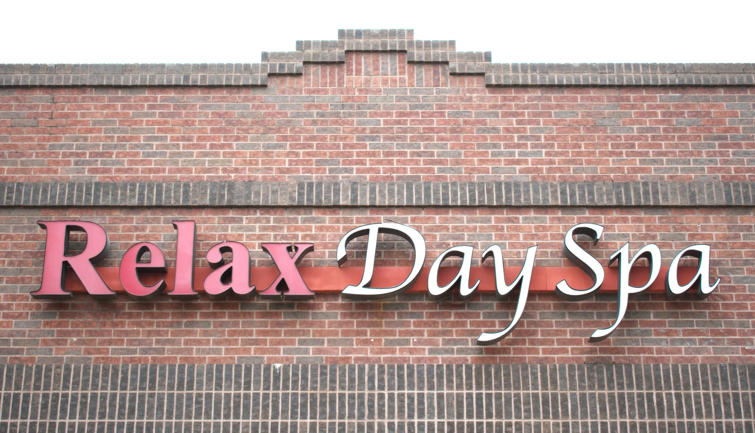 Sign reading "Relax Day Spa" mounted on a brick wall.