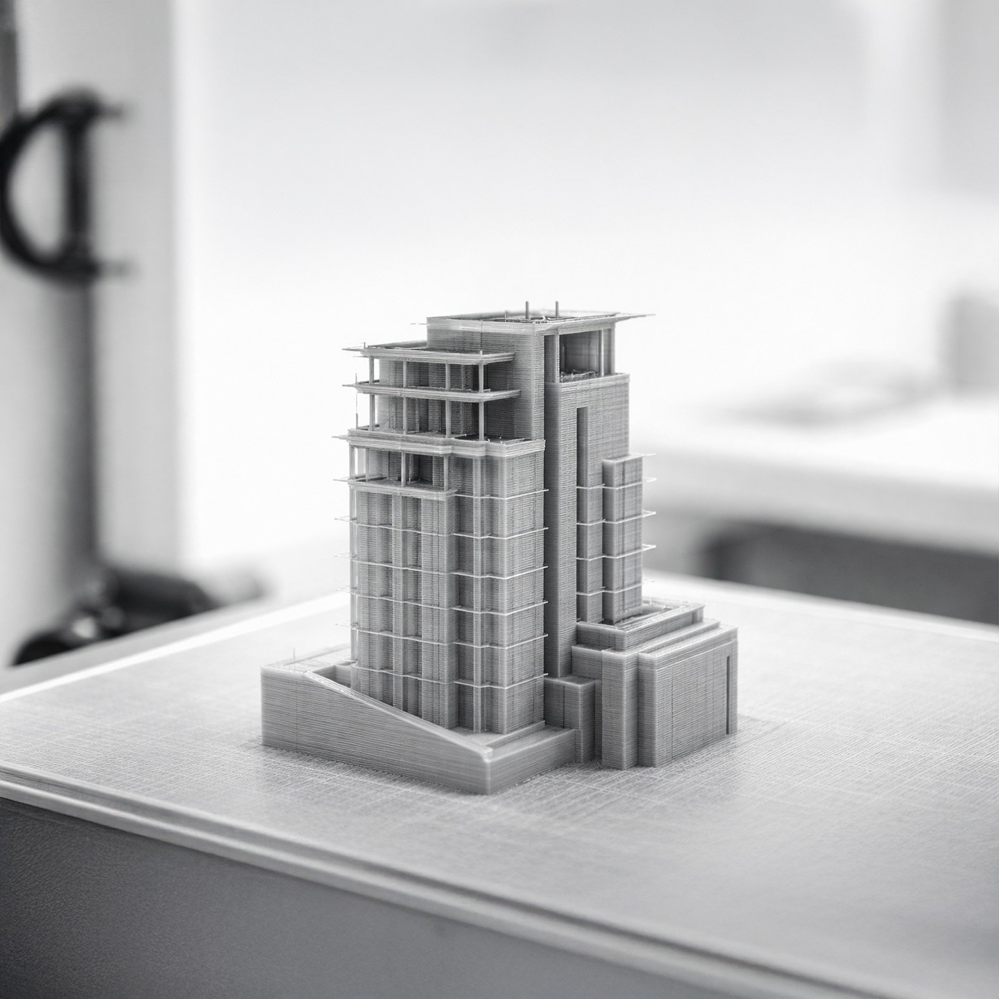 Monochrome gray 3D printed architectural prototype mid-print in a clean prototyping environment.