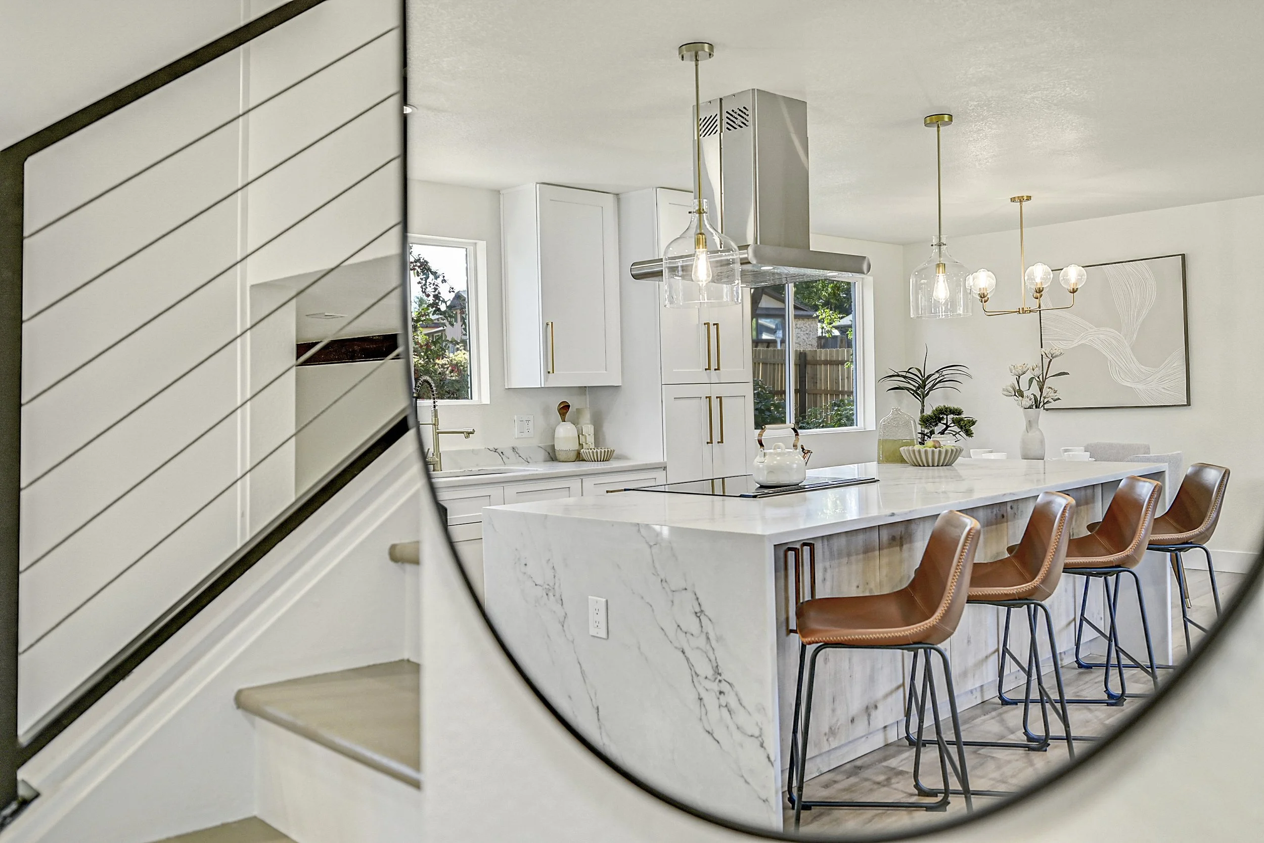Modern white kitchen with marble island, brown bar stools, pendant lighting, and decorative vases with flowers.