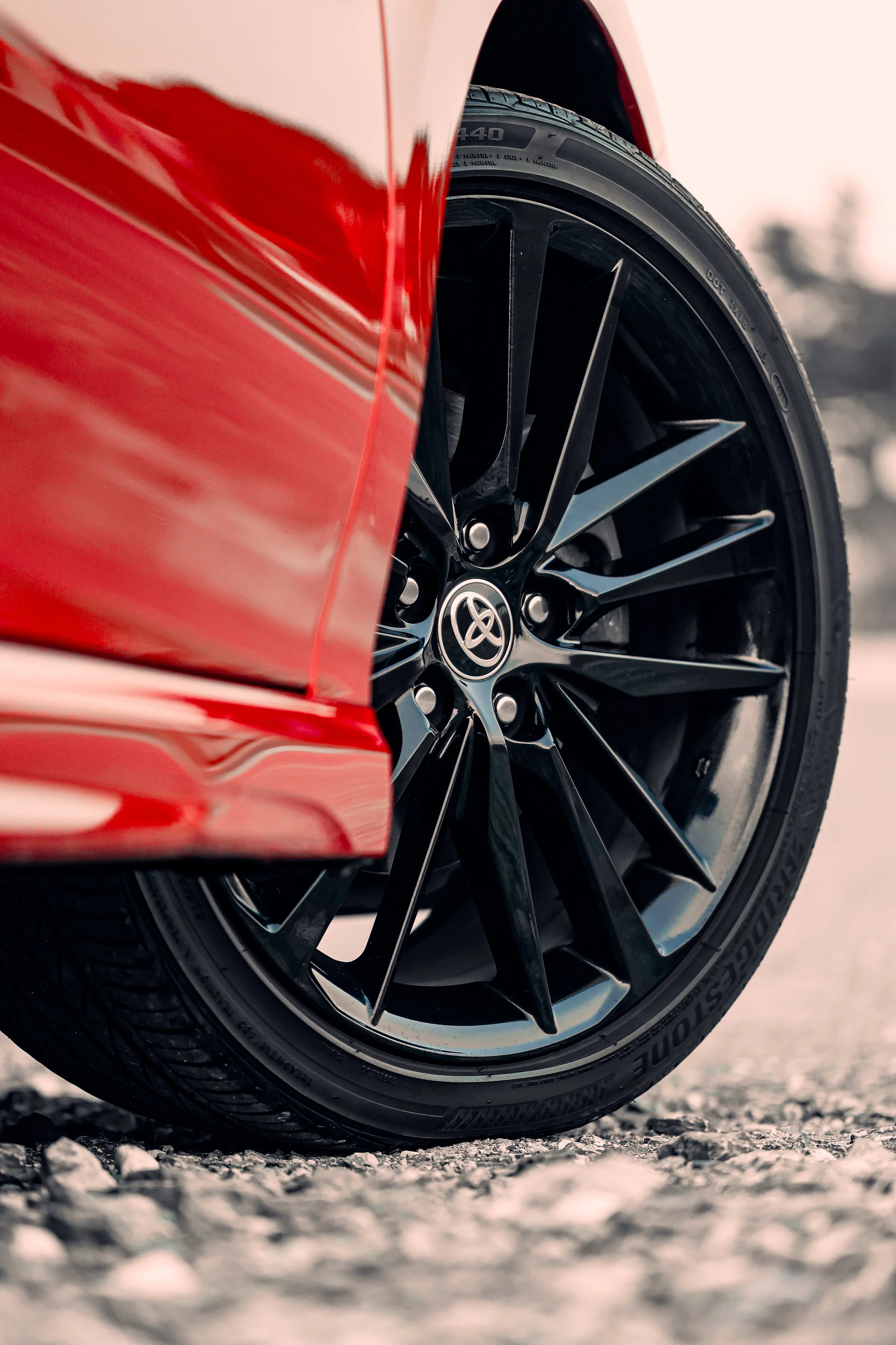 Close-up of a red sports car wheel with a black alloy rim, parked on gravel.