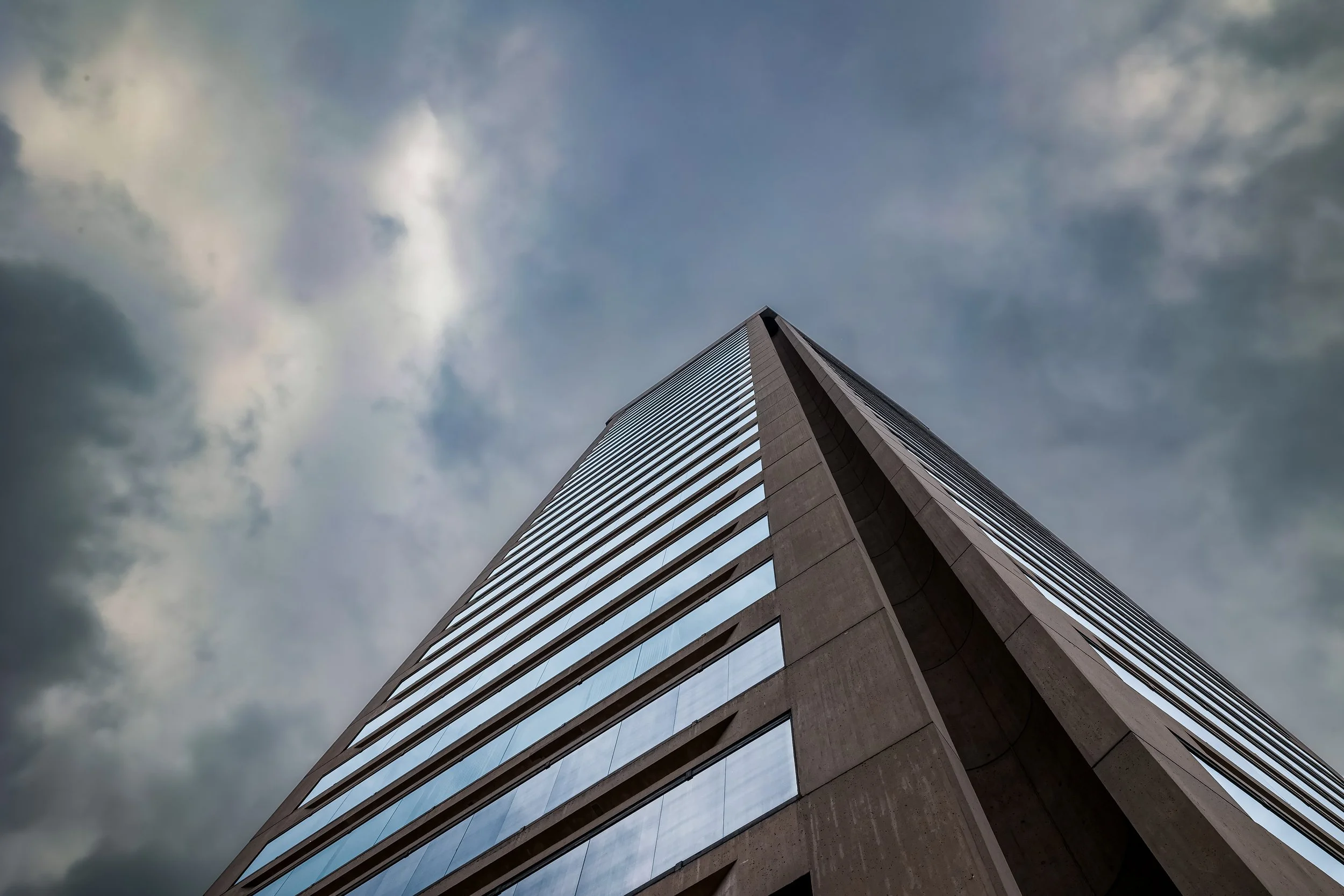 A tall modern skyscraper viewed from below against a cloudy sky.