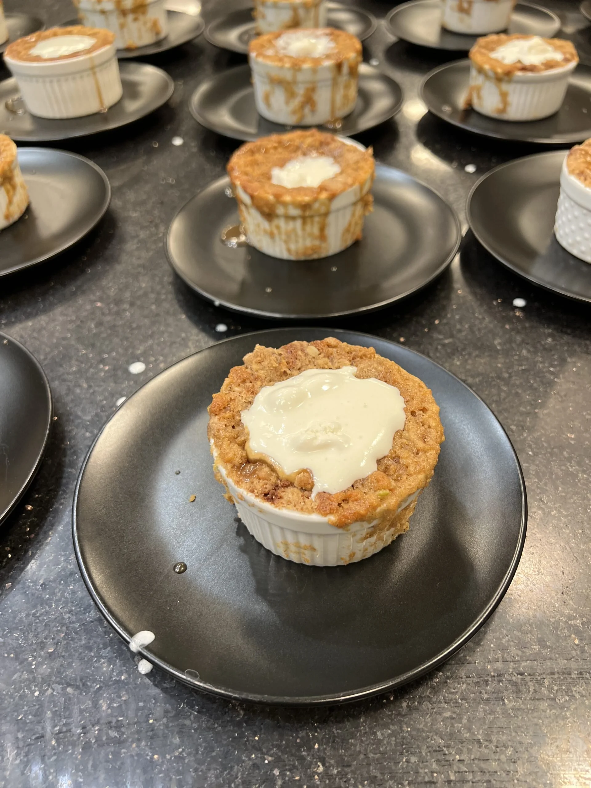 Individual servings of apple crumble topped with a dollop of cream, placed on black plates.